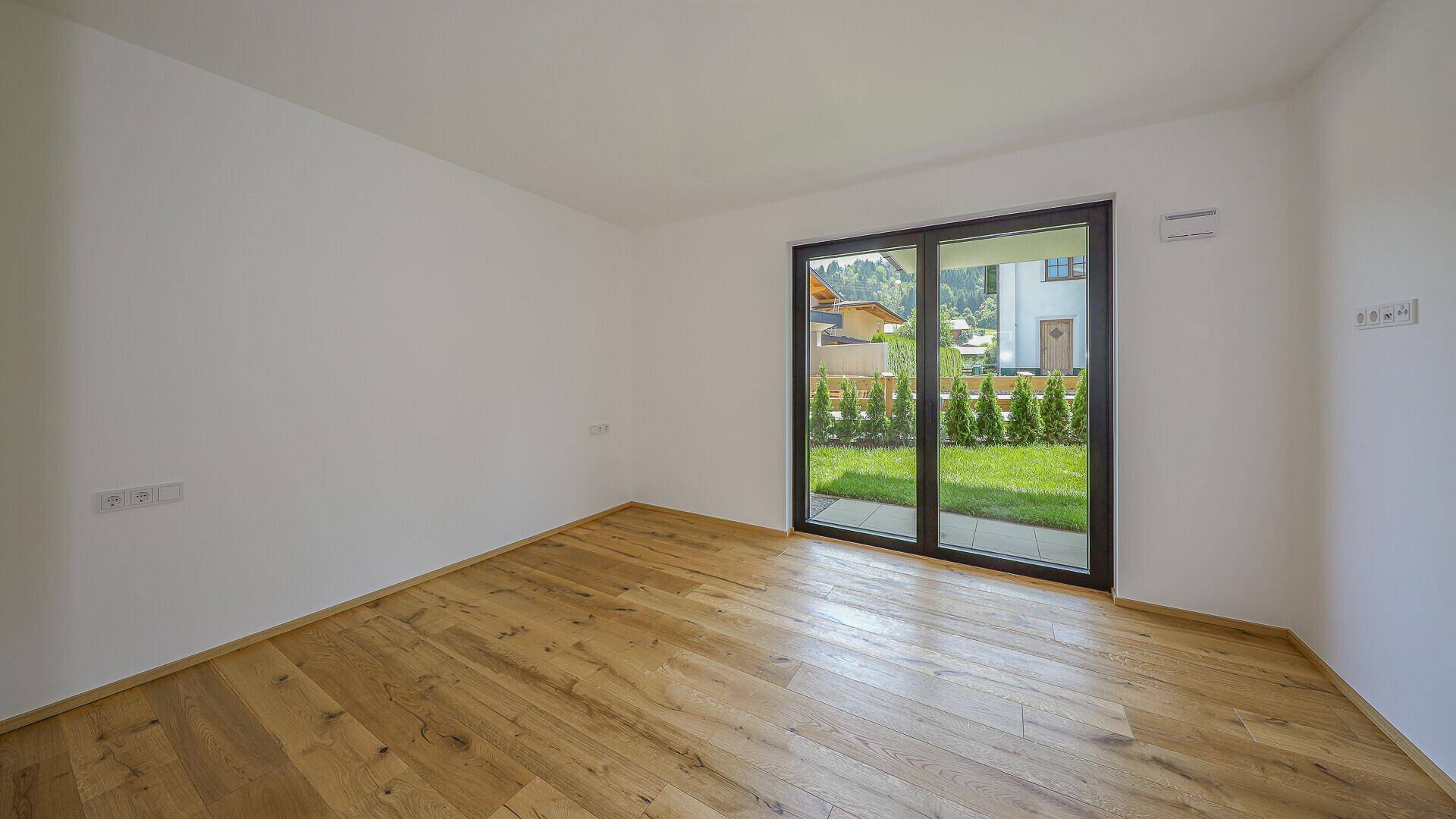 Heller, unmöblierter Raum mit Holzboden und Blick auf den Garten.