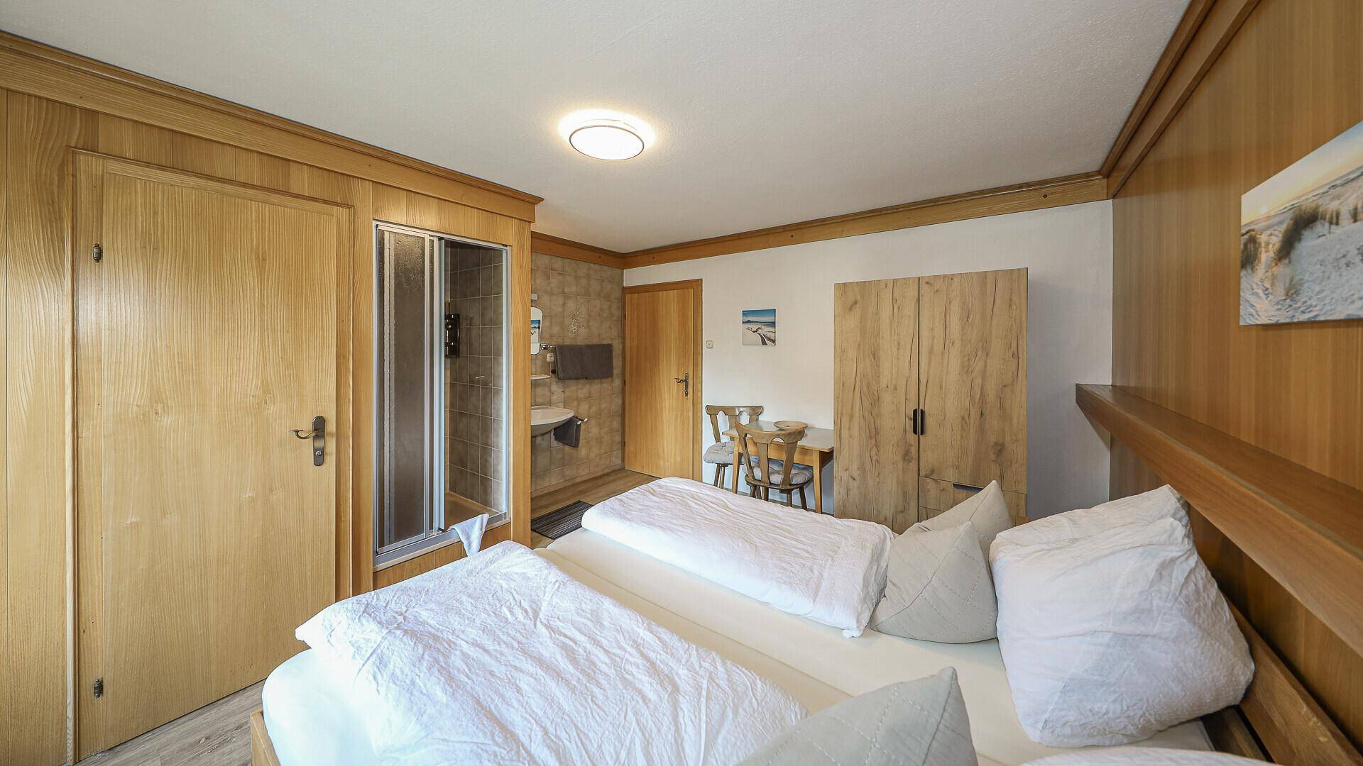 Schlafzimmer mit Holzvertäfelung, Doppelbett und integriertem Duschbereich mit Waschbecken.