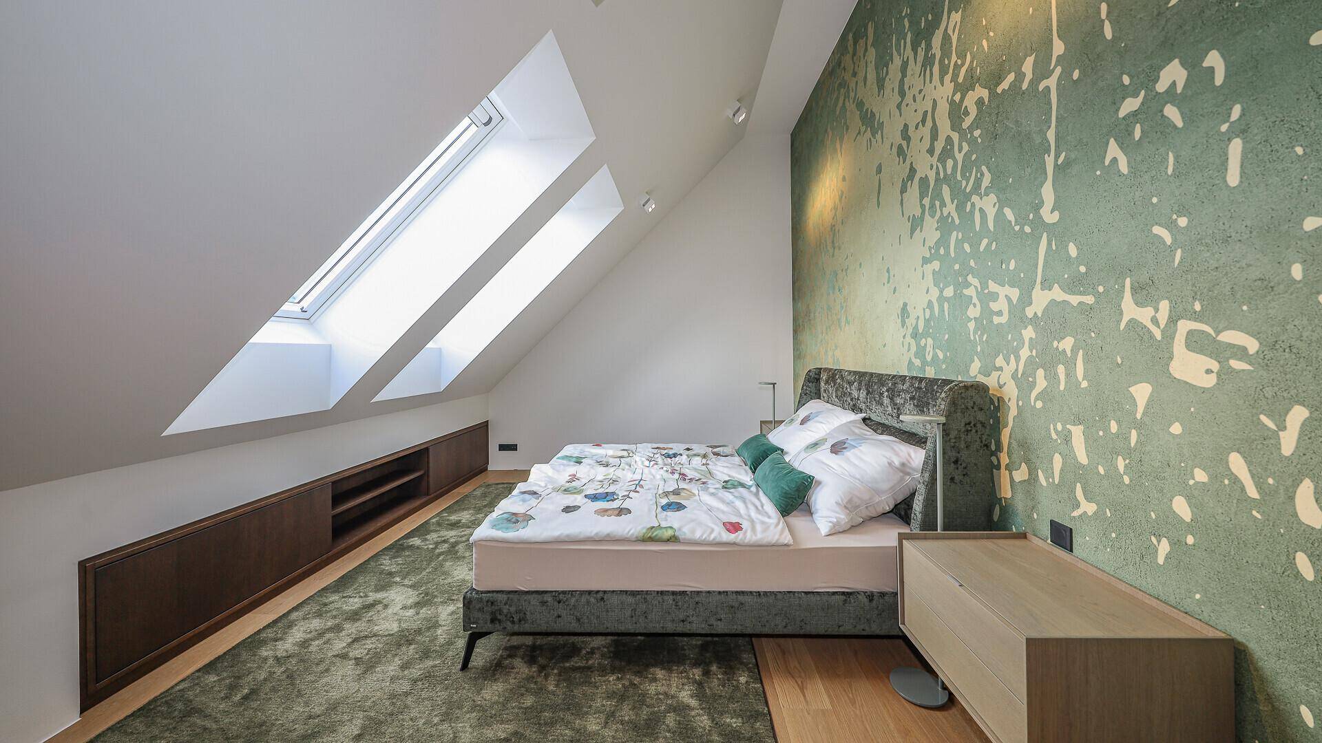 Helles Schlafzimmer im Dachgeschoss mit zwei Dachfenstern, grüner Wand und Holzboden.