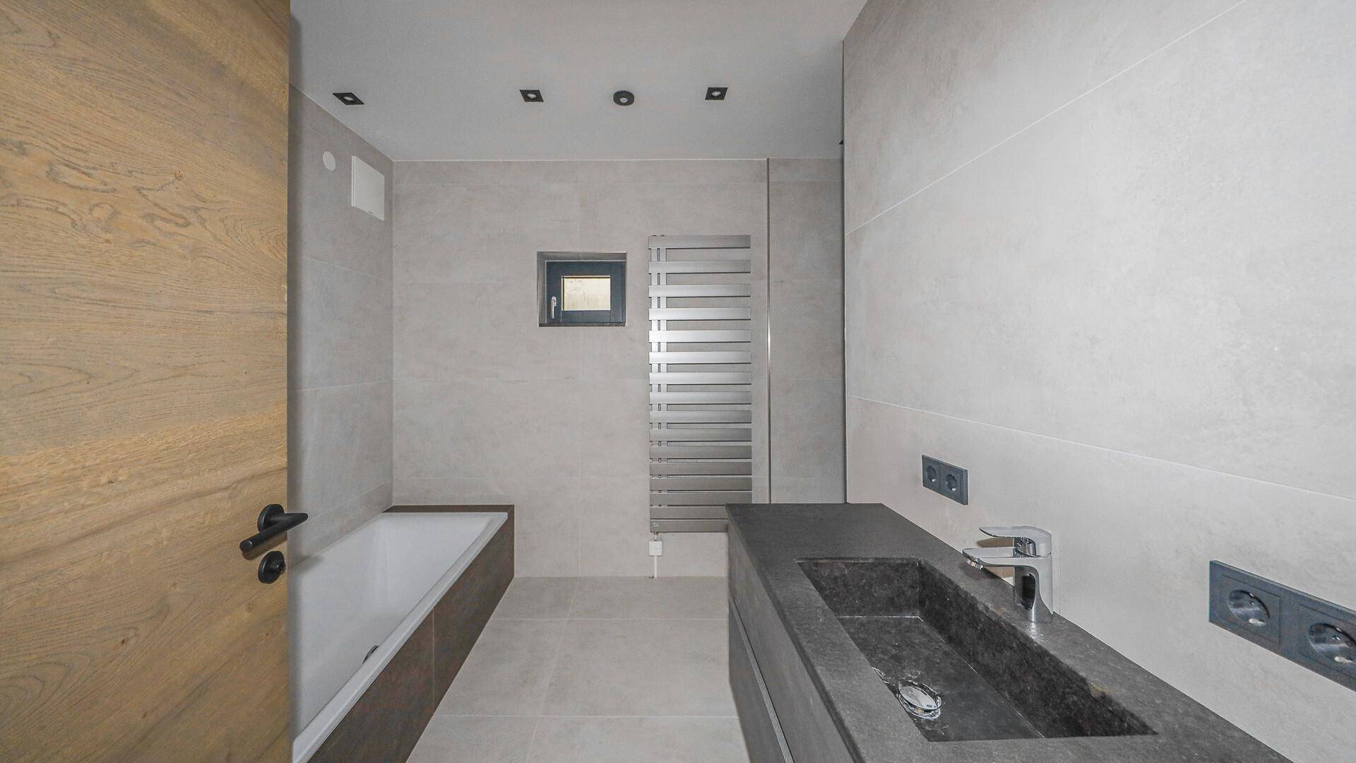 Modernes Badezimmer mit Badewanne, dunklem Waschtisch und beheiztem Handtuchhalter.