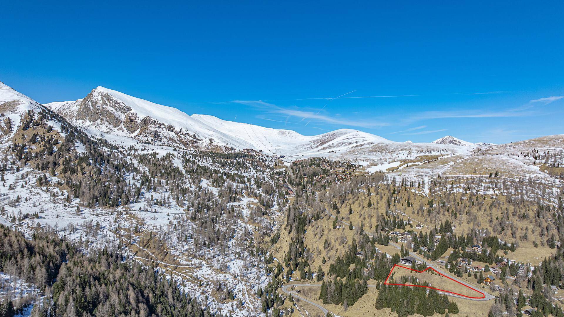 Weitläufige Ansicht einer verschneiten Berglandschaft mit einem markierten Grundstück und vereinzelten Gebäuden.