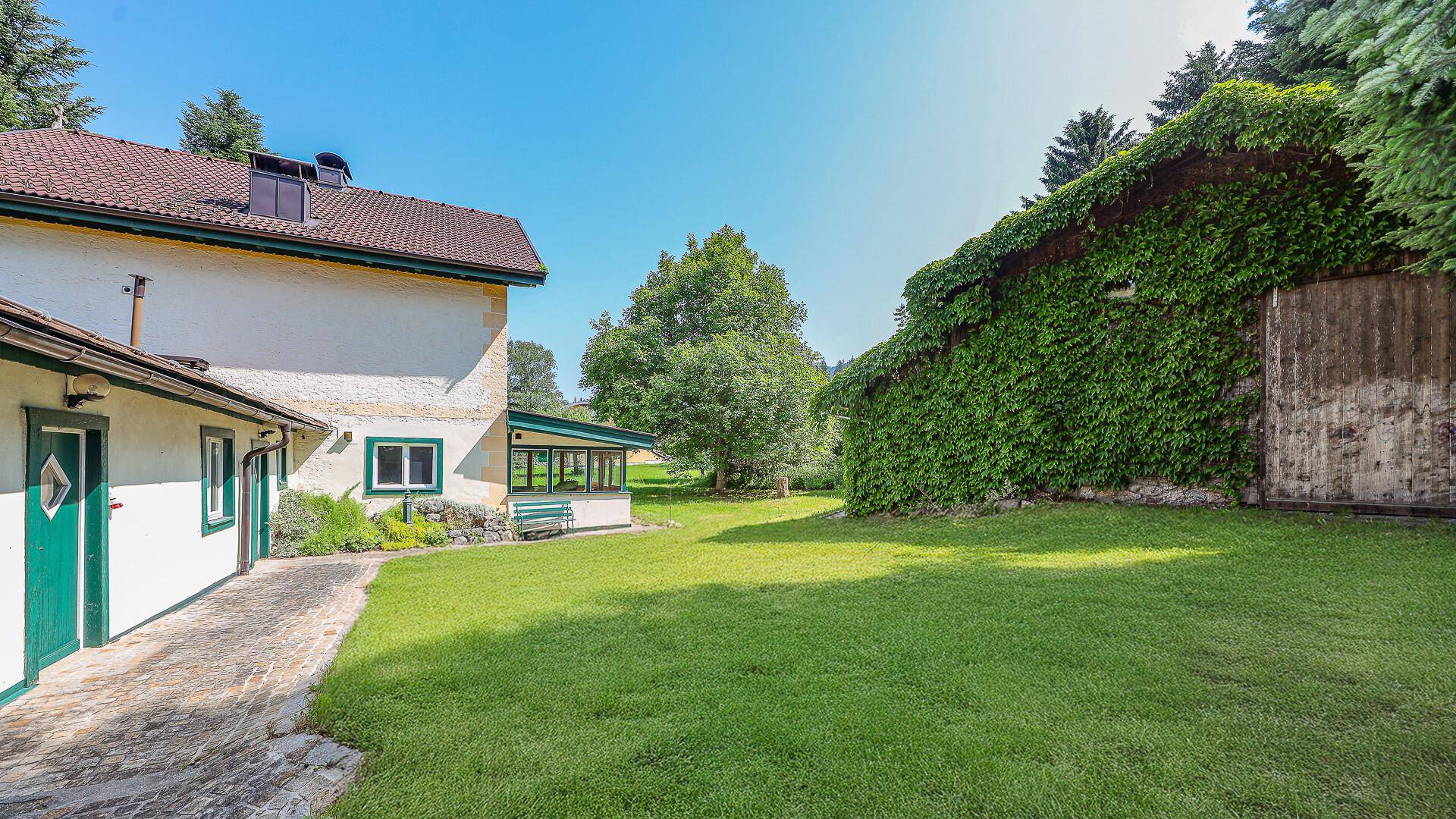 Rückseite des Hauses mit angrenzendem, efeubewachsenem Nebengebäude und weitläufiger Rasenfläche.