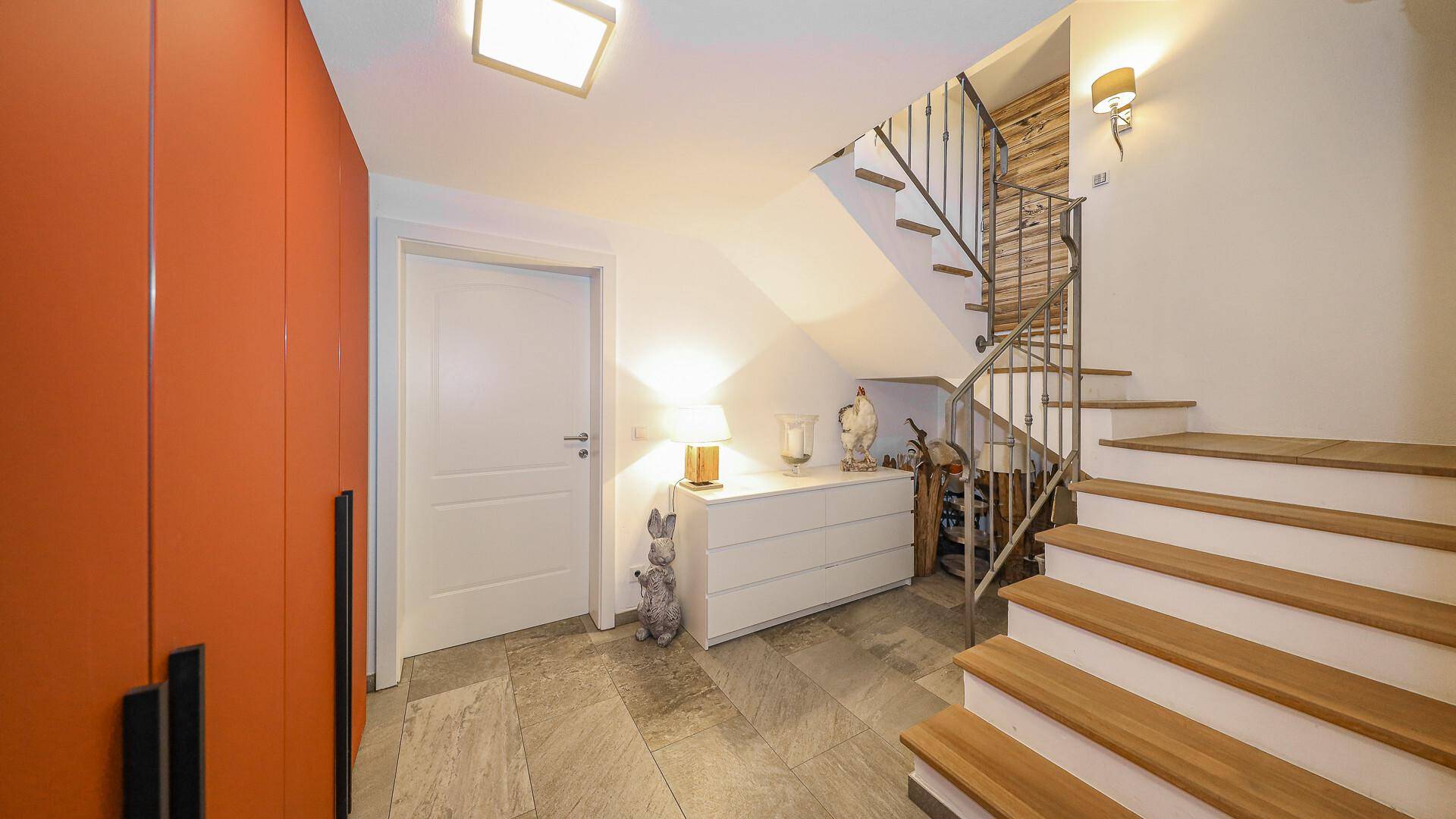 Moderner Flur mit orangefarbenen Schränken, Treppe und heller Beleuchtung.