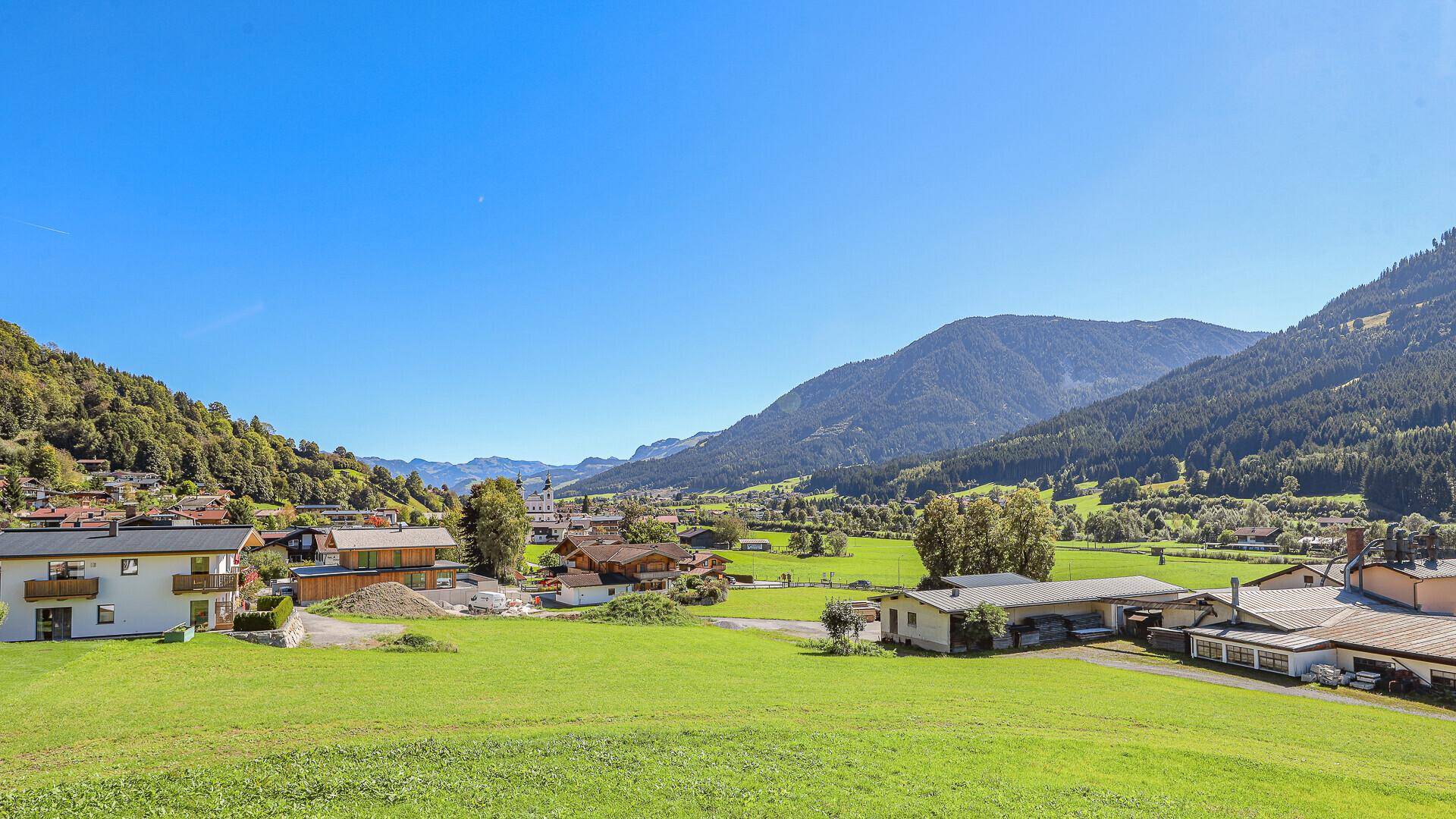 Weitläufige grüne Landschaft mit Bergen und traditionellen Häusern unter blauem Himmel.