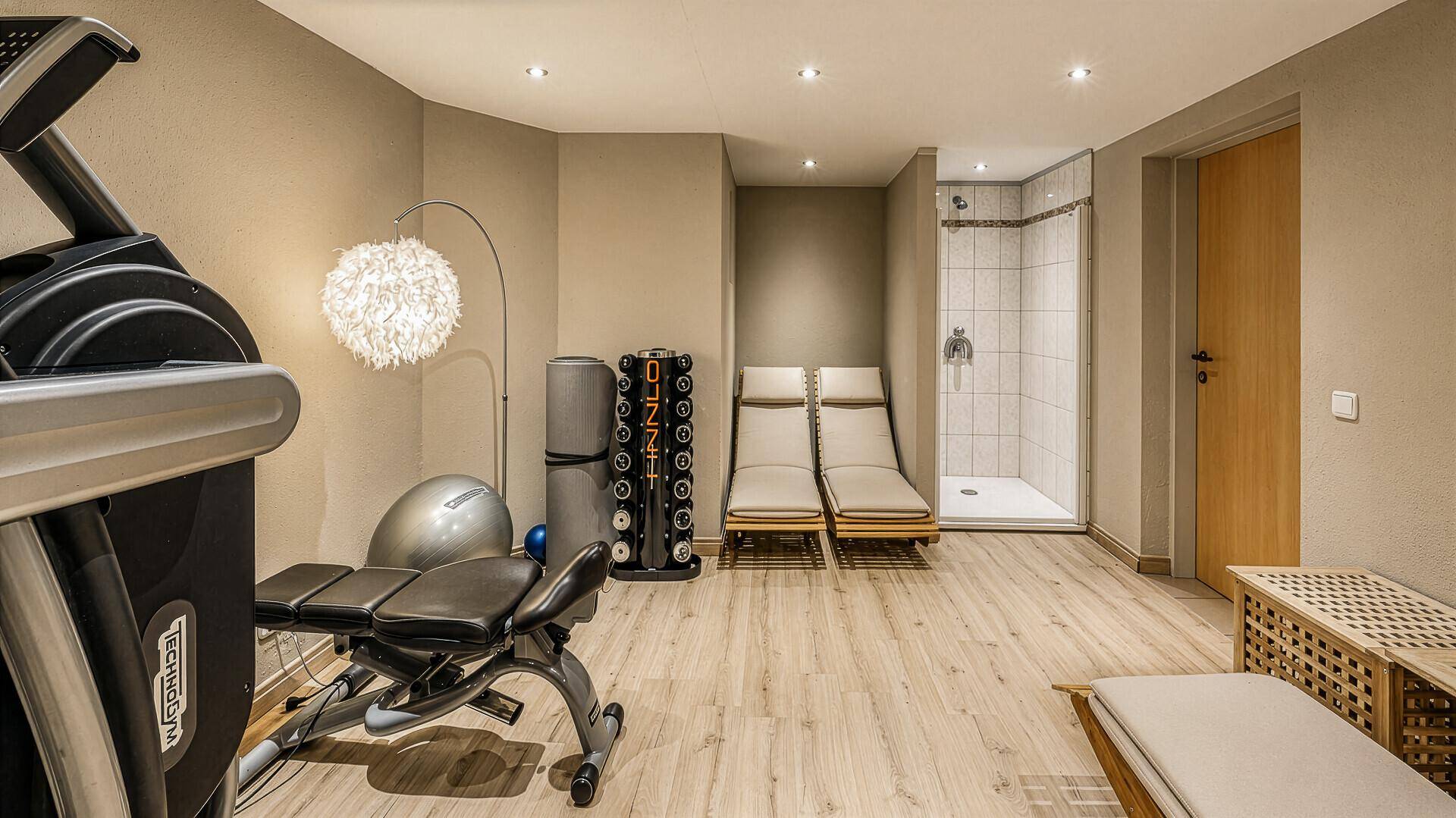Gut ausgestatteter Fitnessraum mit Trainingsgeräten, Liegen und integrierter Dusche.