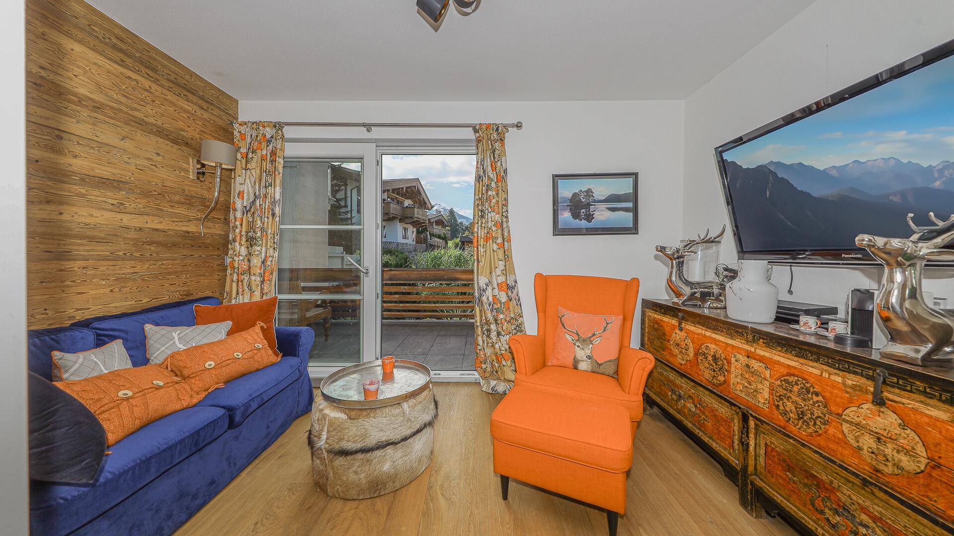 Gemütliches Wohnzimmer mit Sofa, Sessel und Zugang zu einem kleinen Balkon.