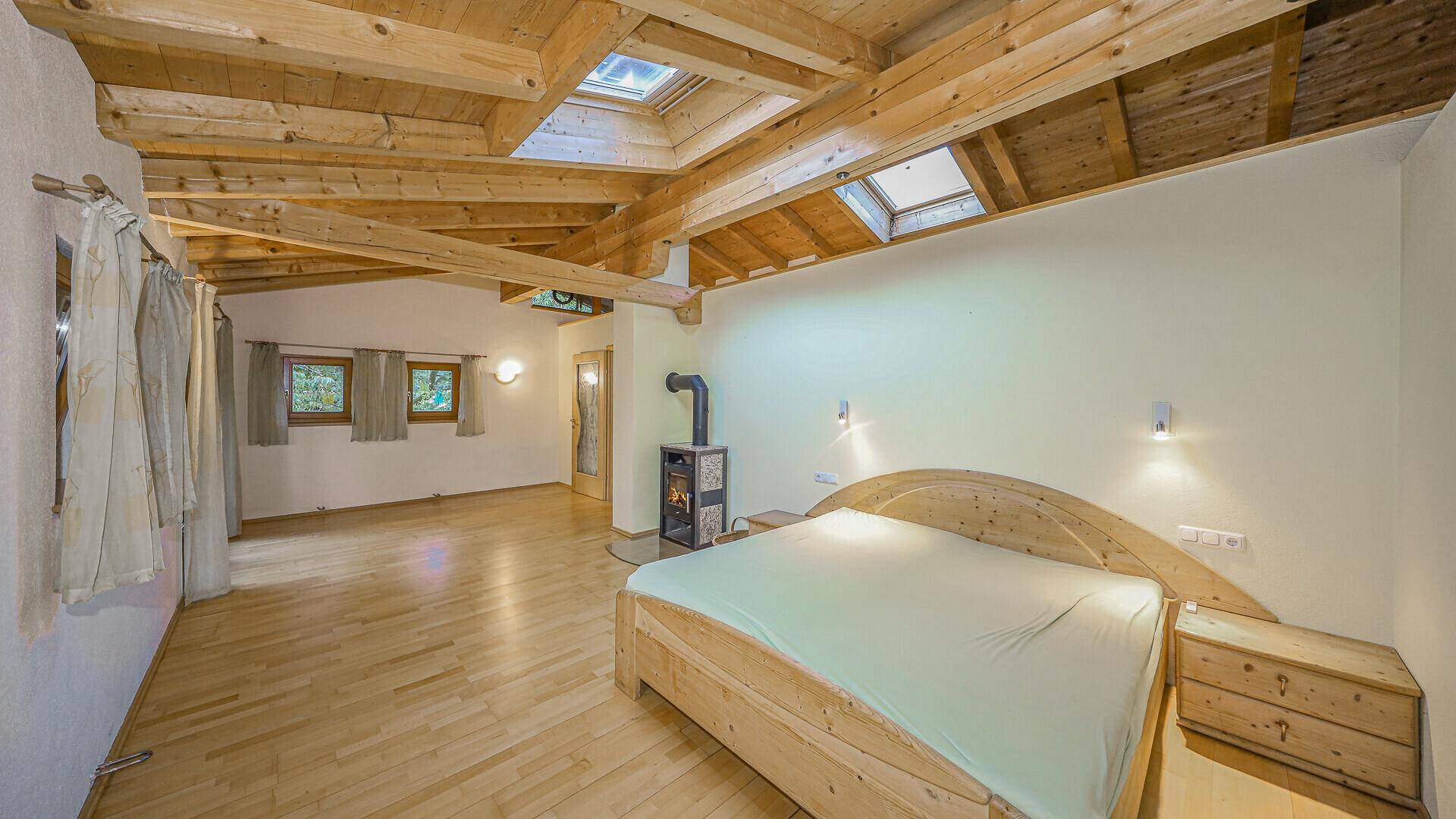 Geräumiges Schlafzimmer mit Holzbalkendecke, Dachfenstern und einem Holzofen, hell und einladend.