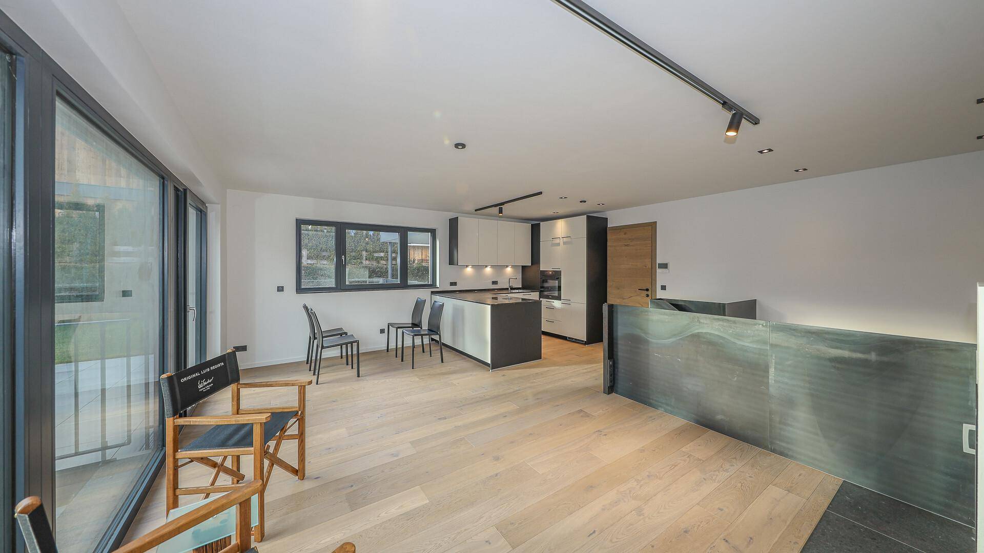 Offener Wohnbereich mit moderner Küche, Holzboden und Zugang zu einem Balkon.