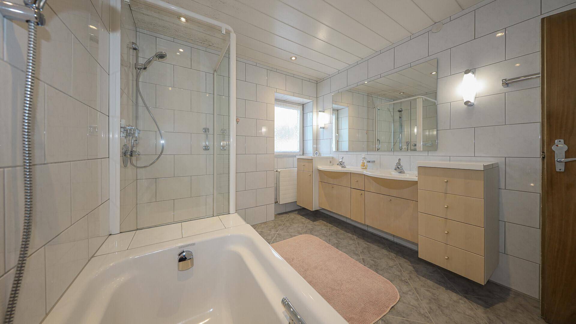 Helles Badezimmer mit Badewanne, Dusche, Doppelwaschbecken und großem Spiegel.