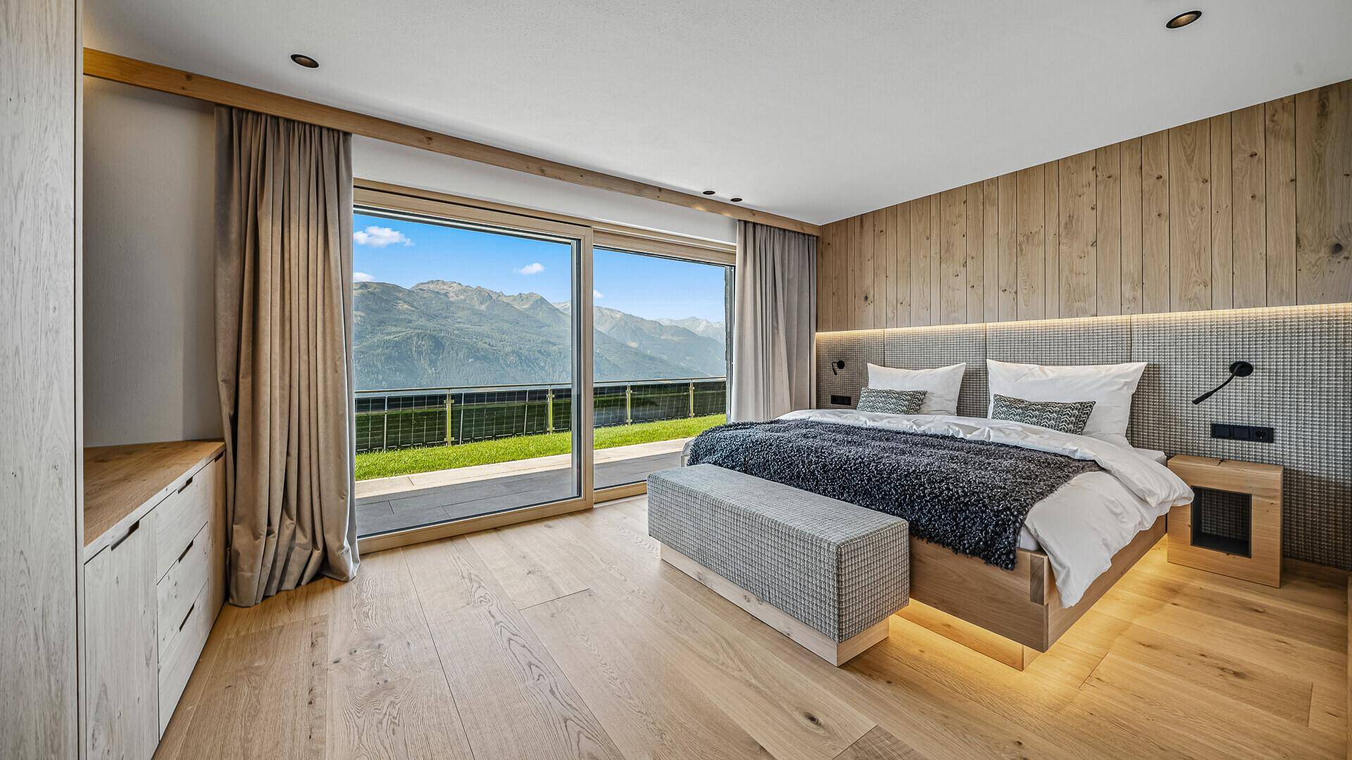 Schlafzimmer mit Holzwand, großem Bett und Zugang zur Terrasse mit Bergblick.