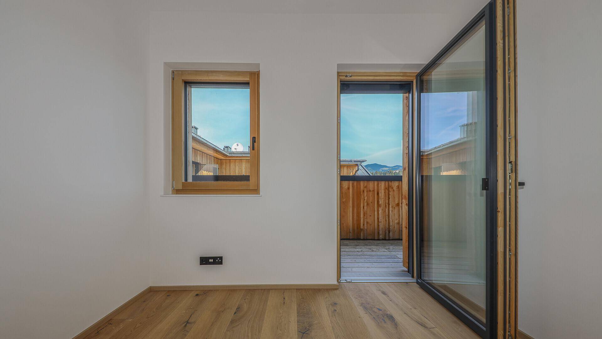 Kleiner, heller Raum mit Holzboden und Zugang zu einem Balkon, ideal als Kinder- oder Gästezimmer.