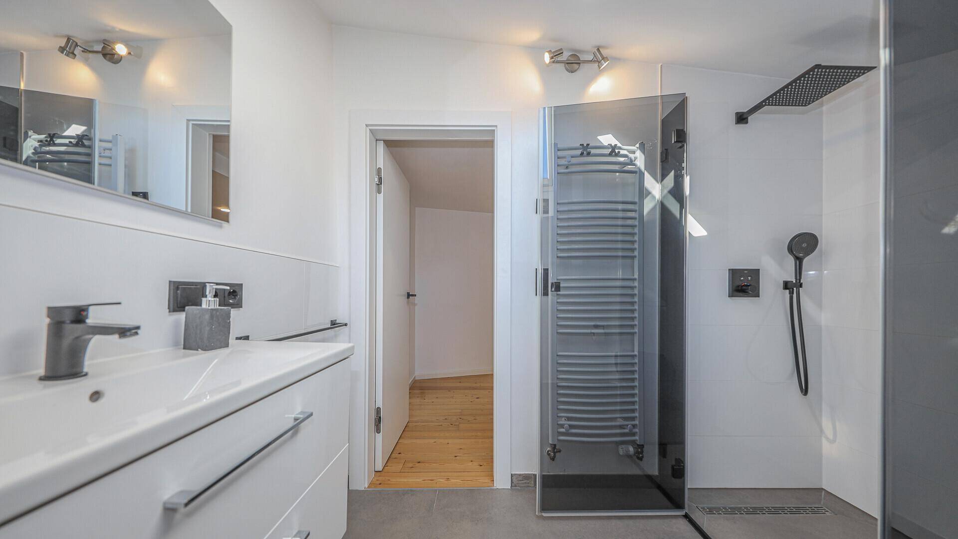 Funktionales Badezimmer mit modernem Waschbecken, beheiztem Handtuchhalter und geräumiger Duschkabine.