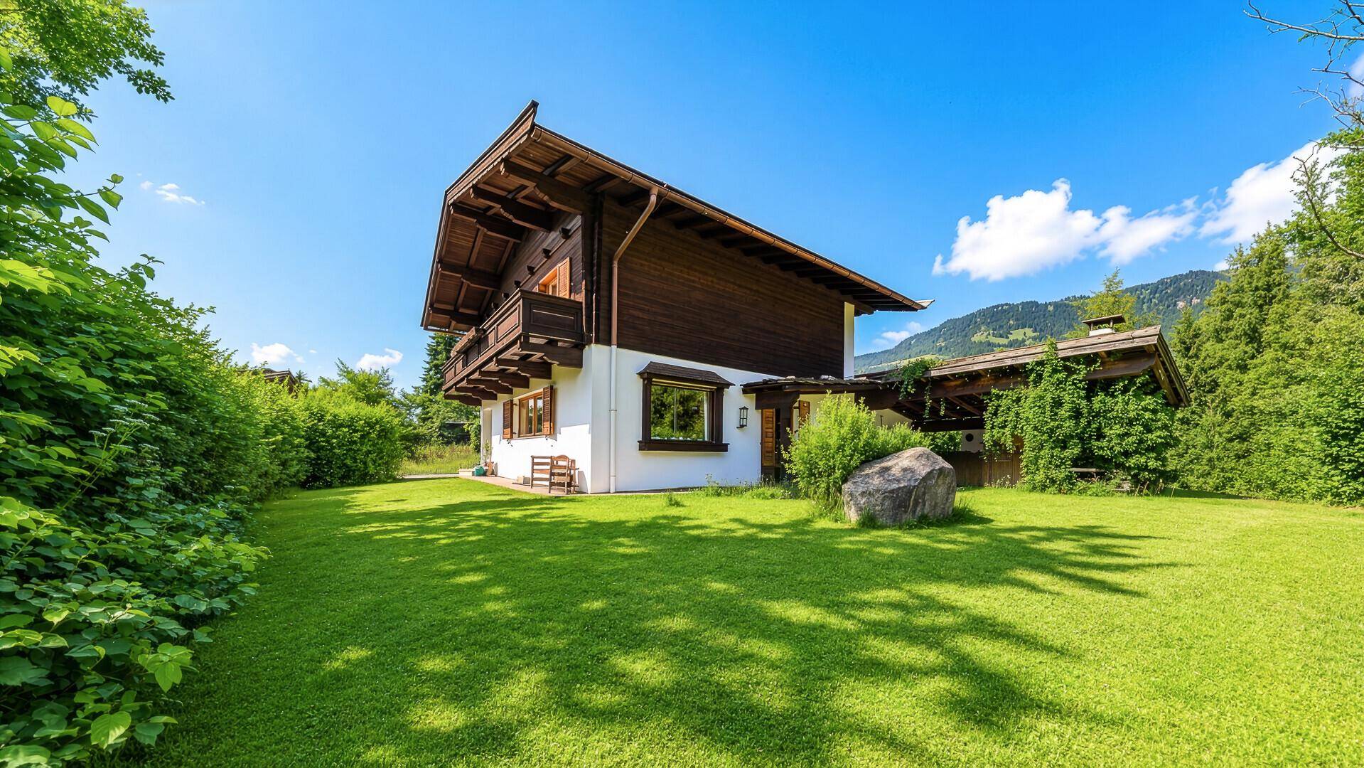 Traditionelles Chalet mit weitläufigem Rasen und Blick auf die umliegende Berglandschaft.