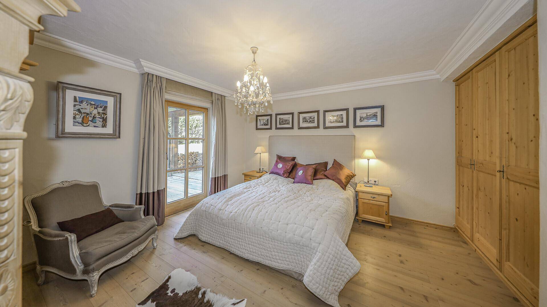 Elegantes Schlafzimmer mit Holzboden, Kronleuchter und Zugang zum Außenbereich.