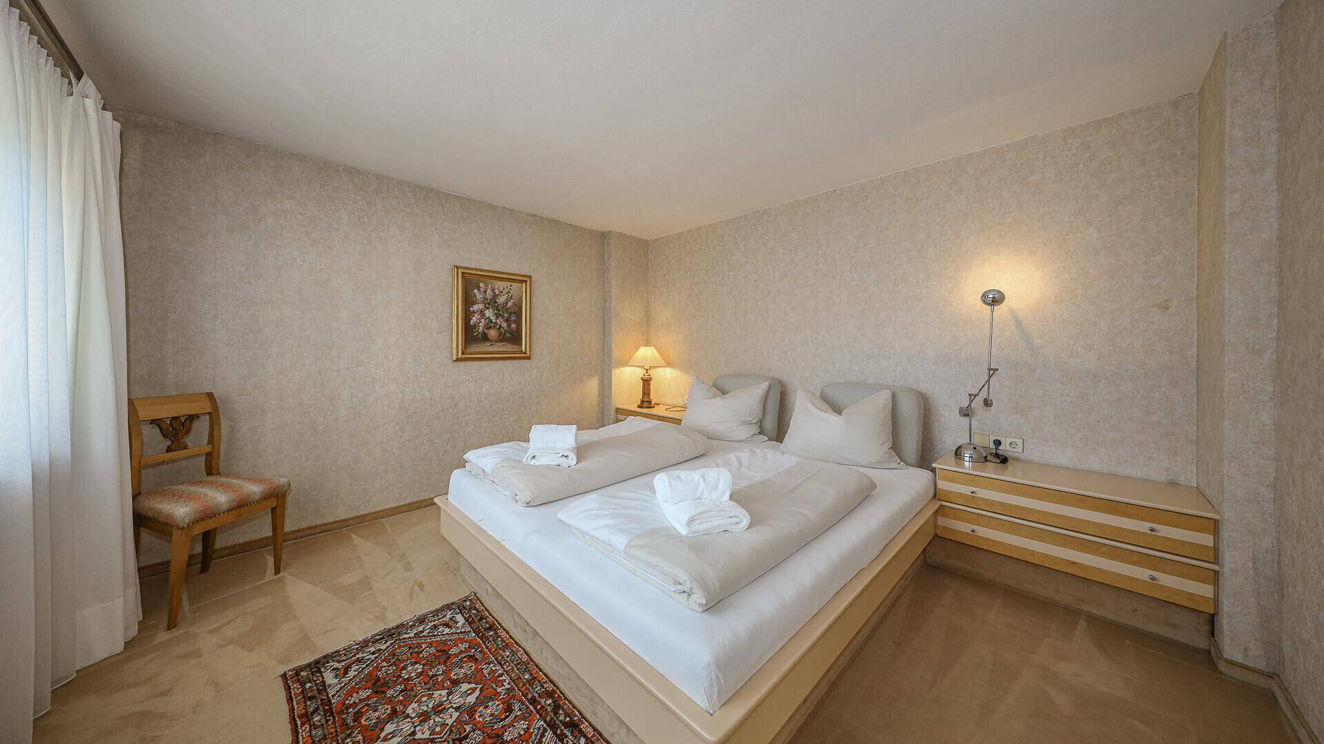 Helles Schlafzimmer mit Doppelbett, Teppichboden und dezenter Tapete.