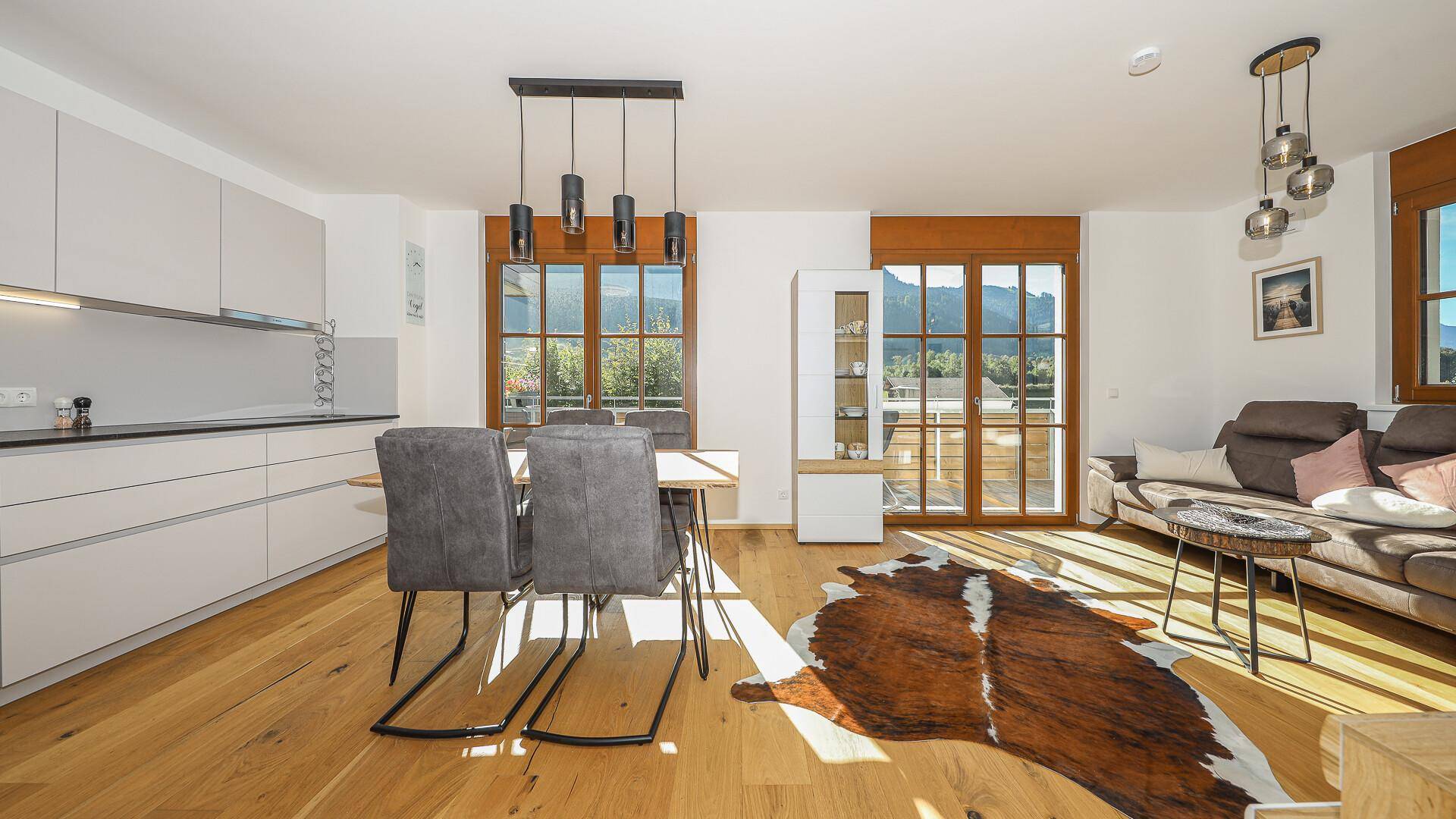Lichtdurchfluteter Wohn-Essbereich mit Holzboden, Esstisch und Zugang zum Balkon.