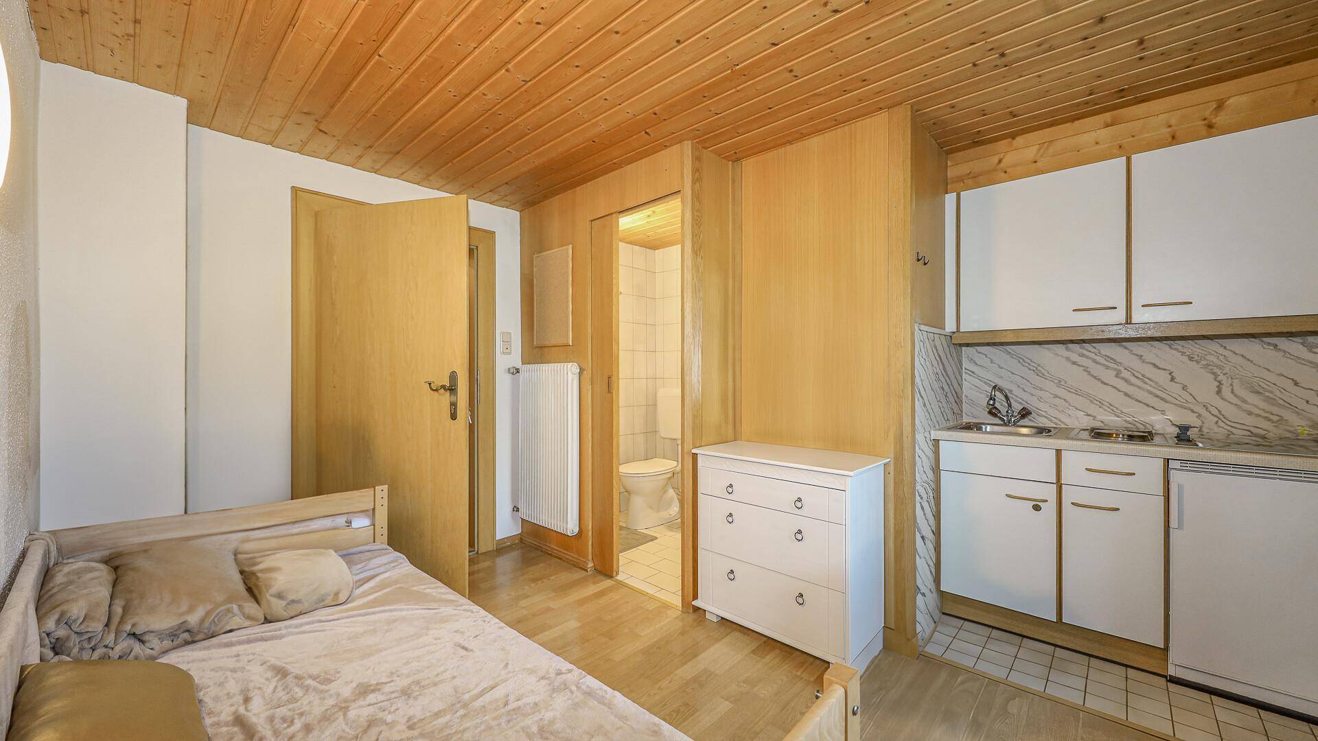 Schlafzimmer mit integrierter Küchenzeile und Zugang zu einem kleinen Badezimmer.