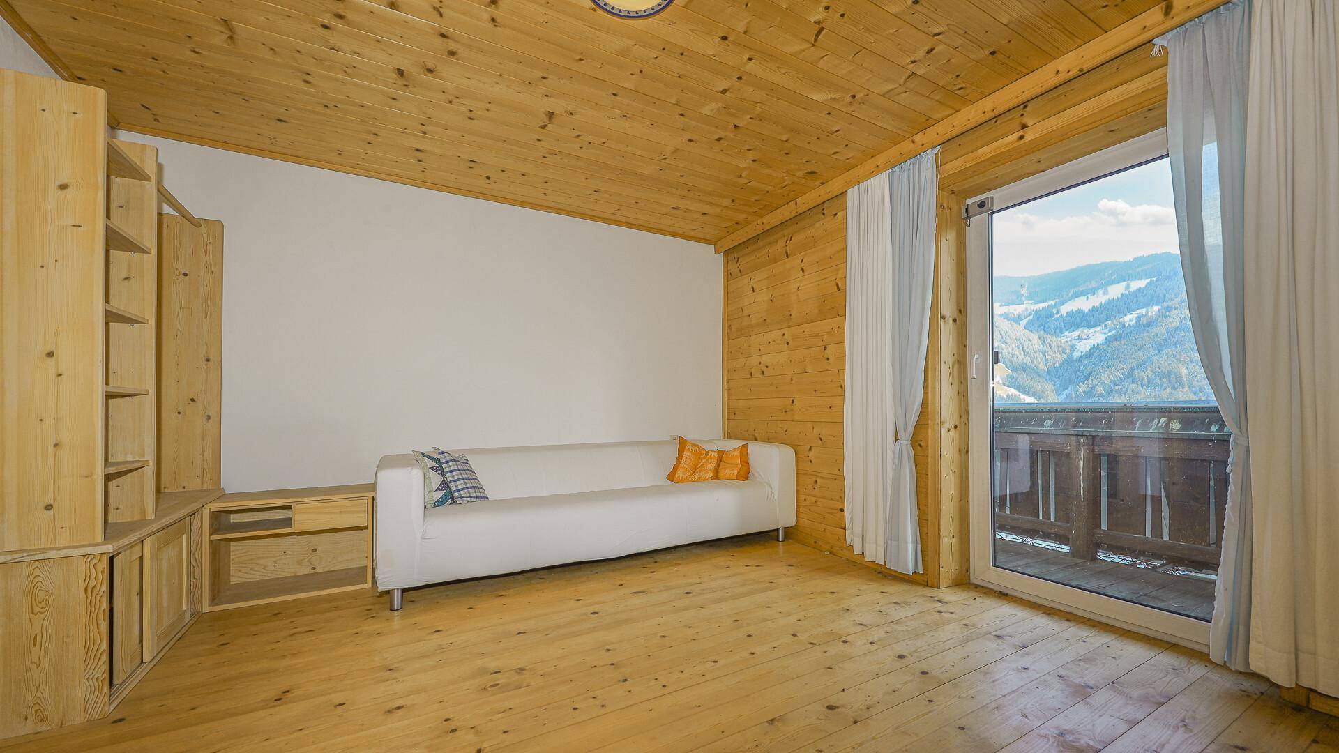 Gemütliches Wohnzimmer mit Holzvertäfelung, Holzdielenboden und Zugang zu einem Balkon mit Bergblick.