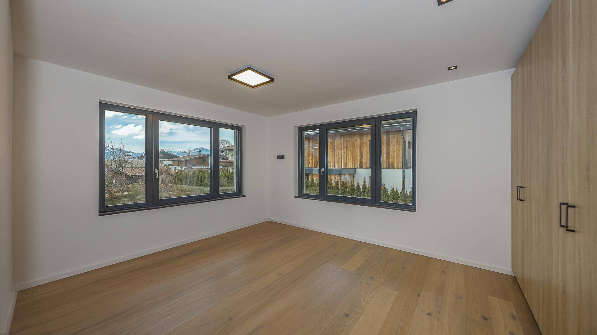 Geräumiges Schlafzimmer mit Holzboden und zwei Fenstern, die viel Tageslicht hereinlassen.