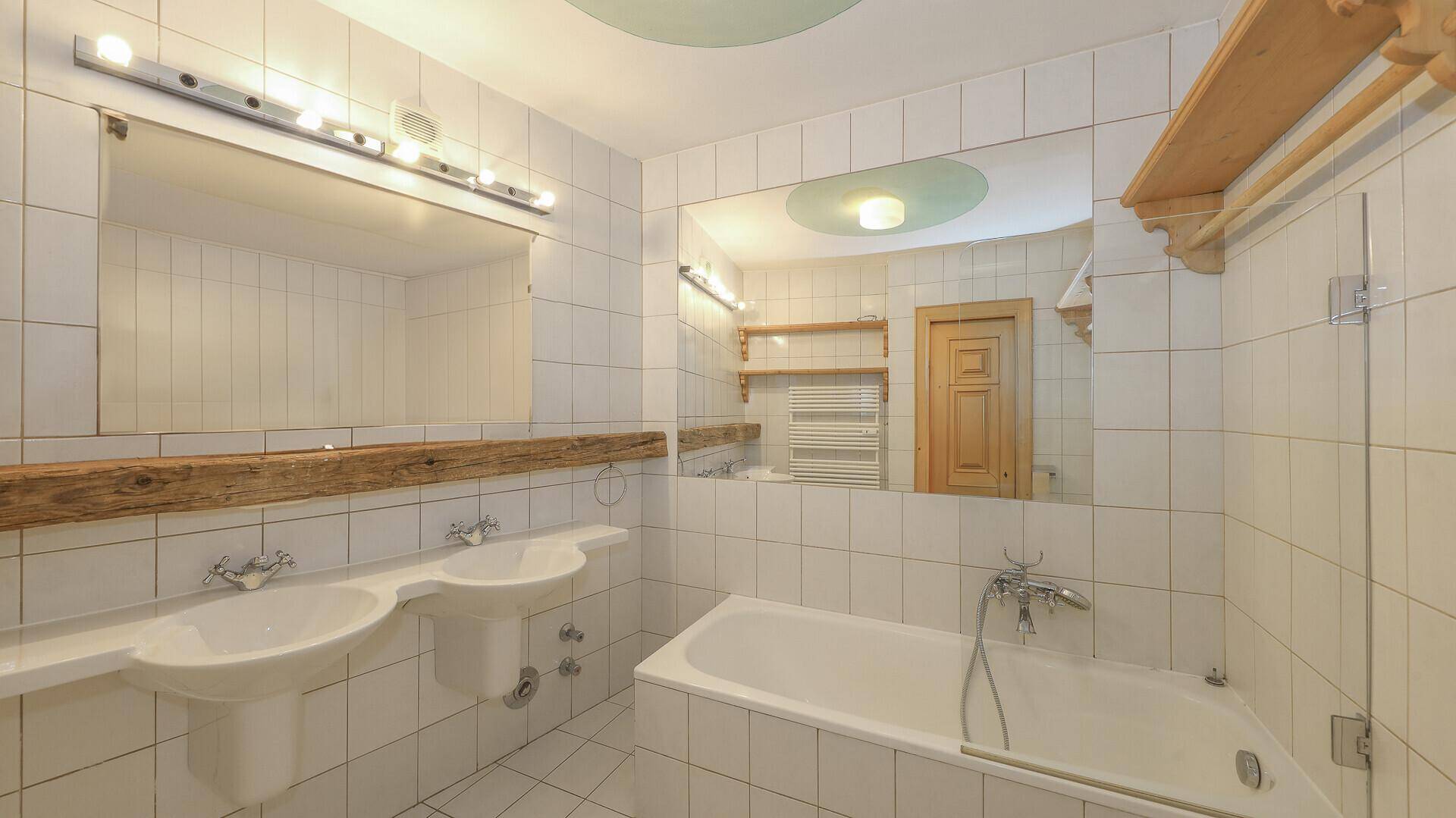 Helles Badezimmer mit weißen Fliesen, Doppelwaschbecken und Badewanne.