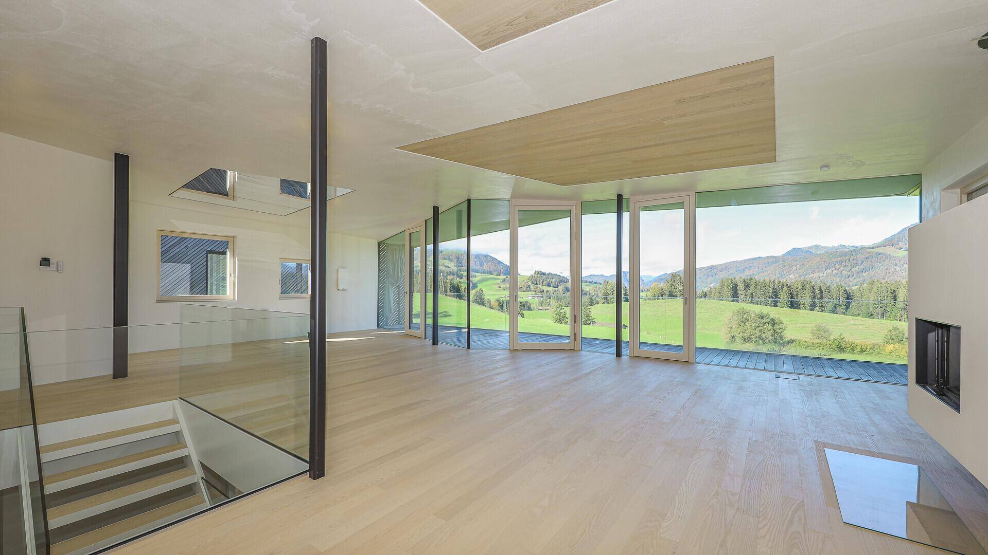 Großzügiger Wohnbereich mit Glasgeländer, Holzboden und Panoramafenstern zur Berglandschaft.