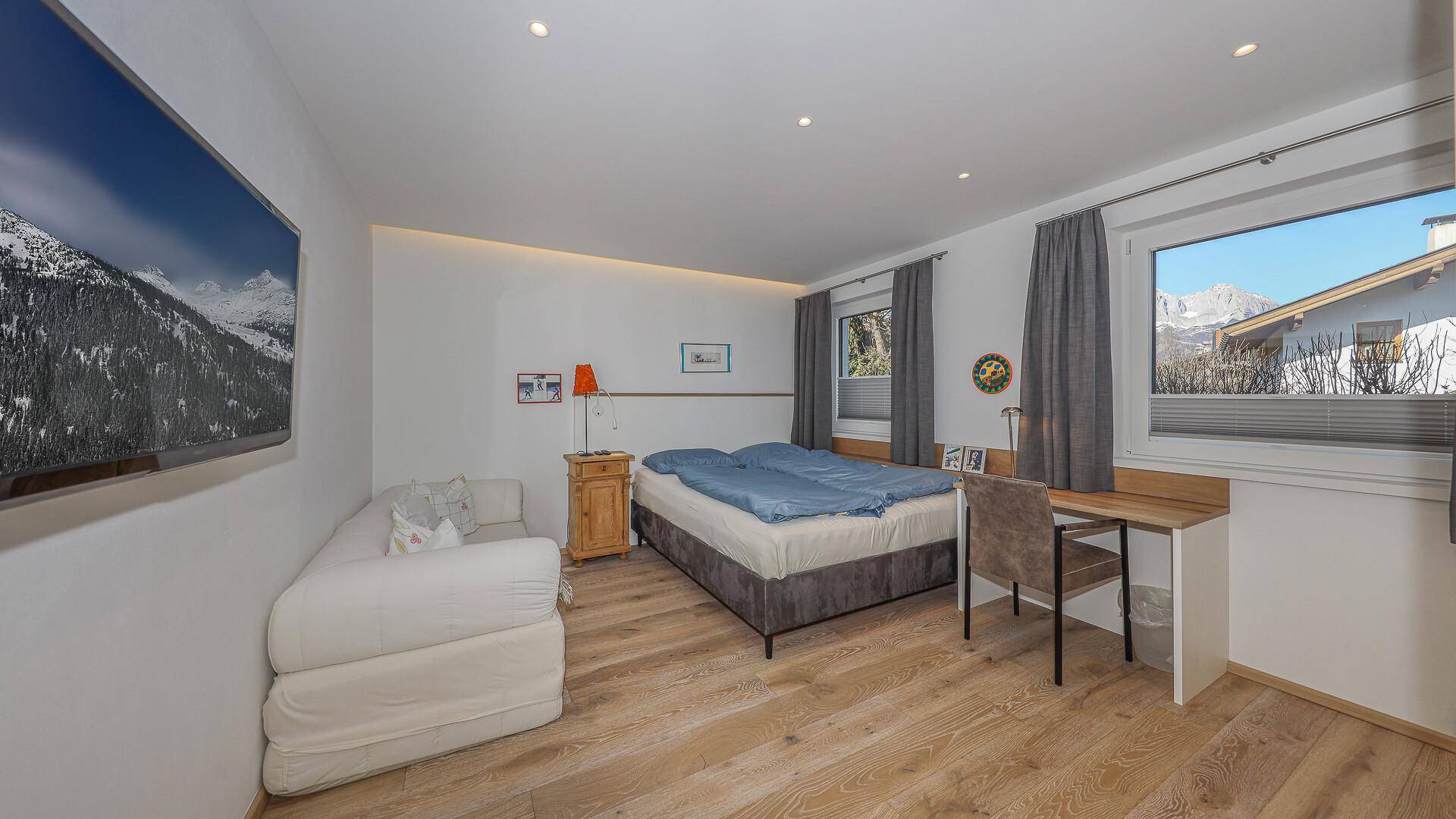 Gemütliches Schlafzimmer mit Doppelbett, Schreibtisch und Bergblick durch das Fenster.