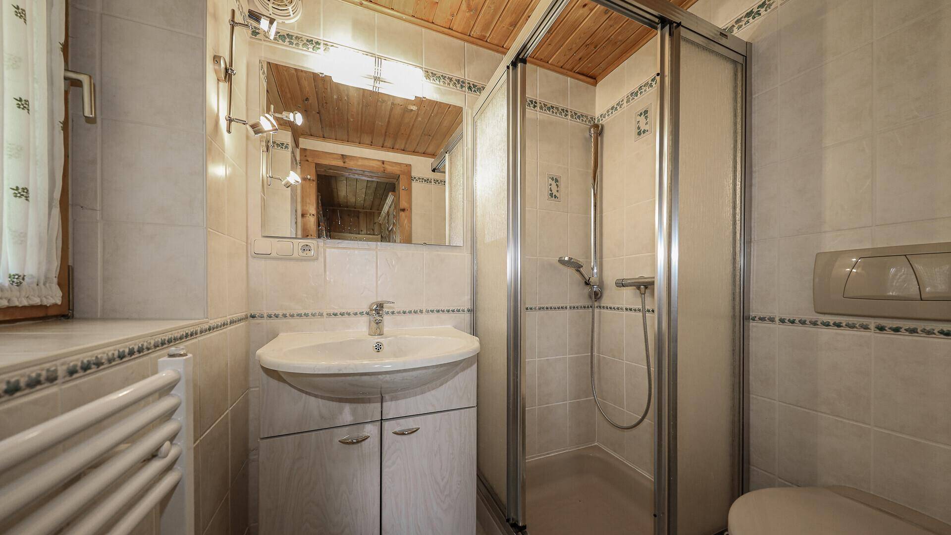 Helles Badezimmer mit weißen Fliesen, Duschkabine, Waschbecken und WC, funktional und sauber.
