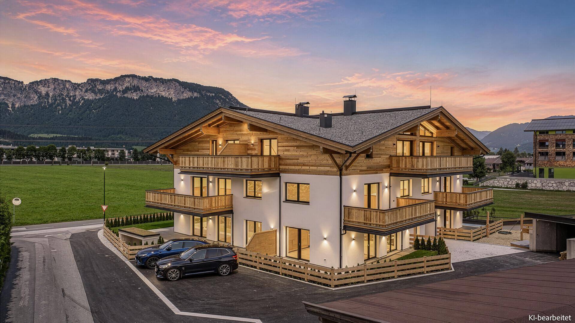 Modernes Mehrfamilienhaus im alpinen Stil bei Sonnenuntergang mit beleuchteten Balkonen.