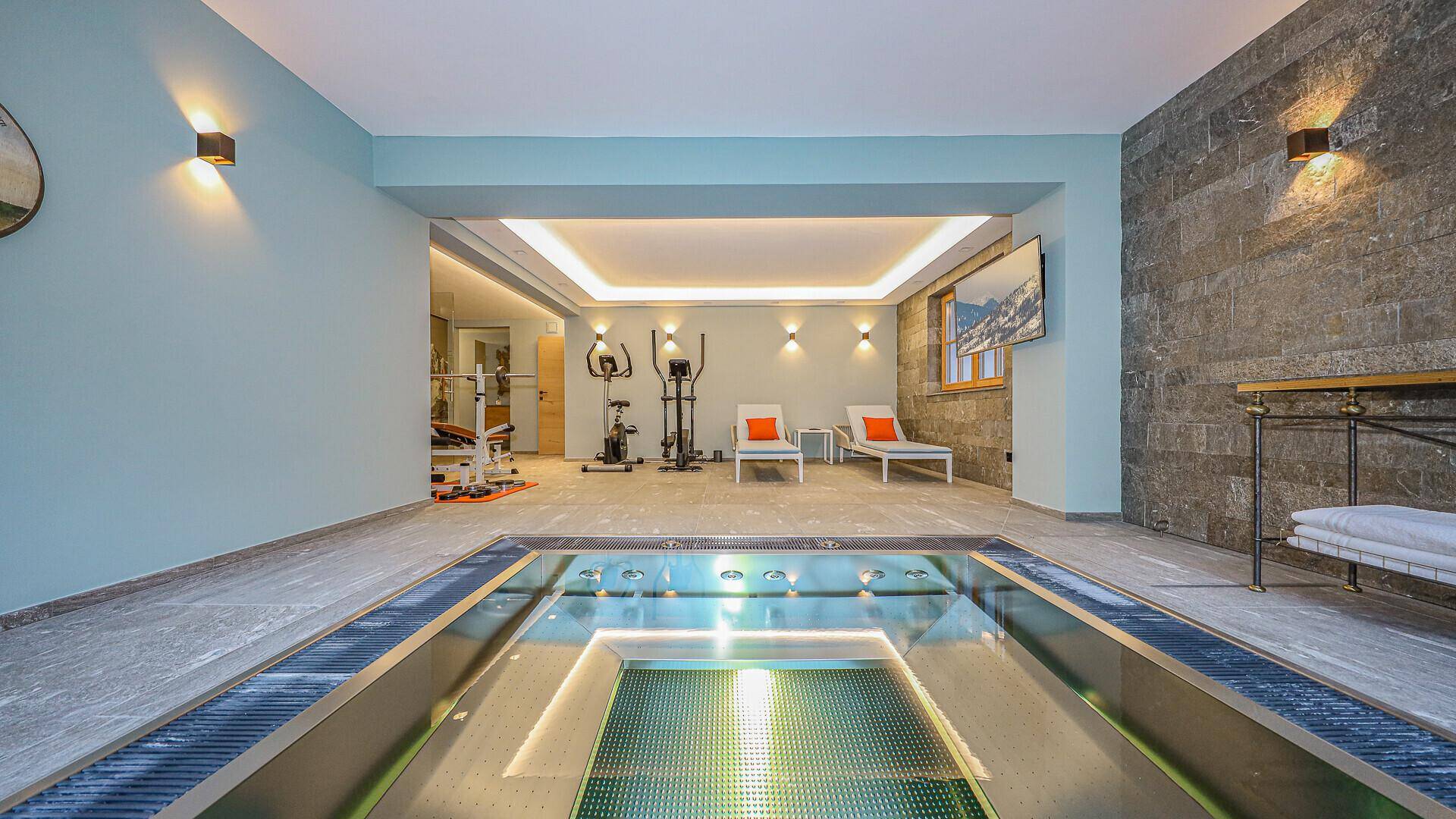 Geräumiger Wellnessbereich mit beleuchtetem Whirlpool und Fitnessgeräten, ideal zur Entspannung.