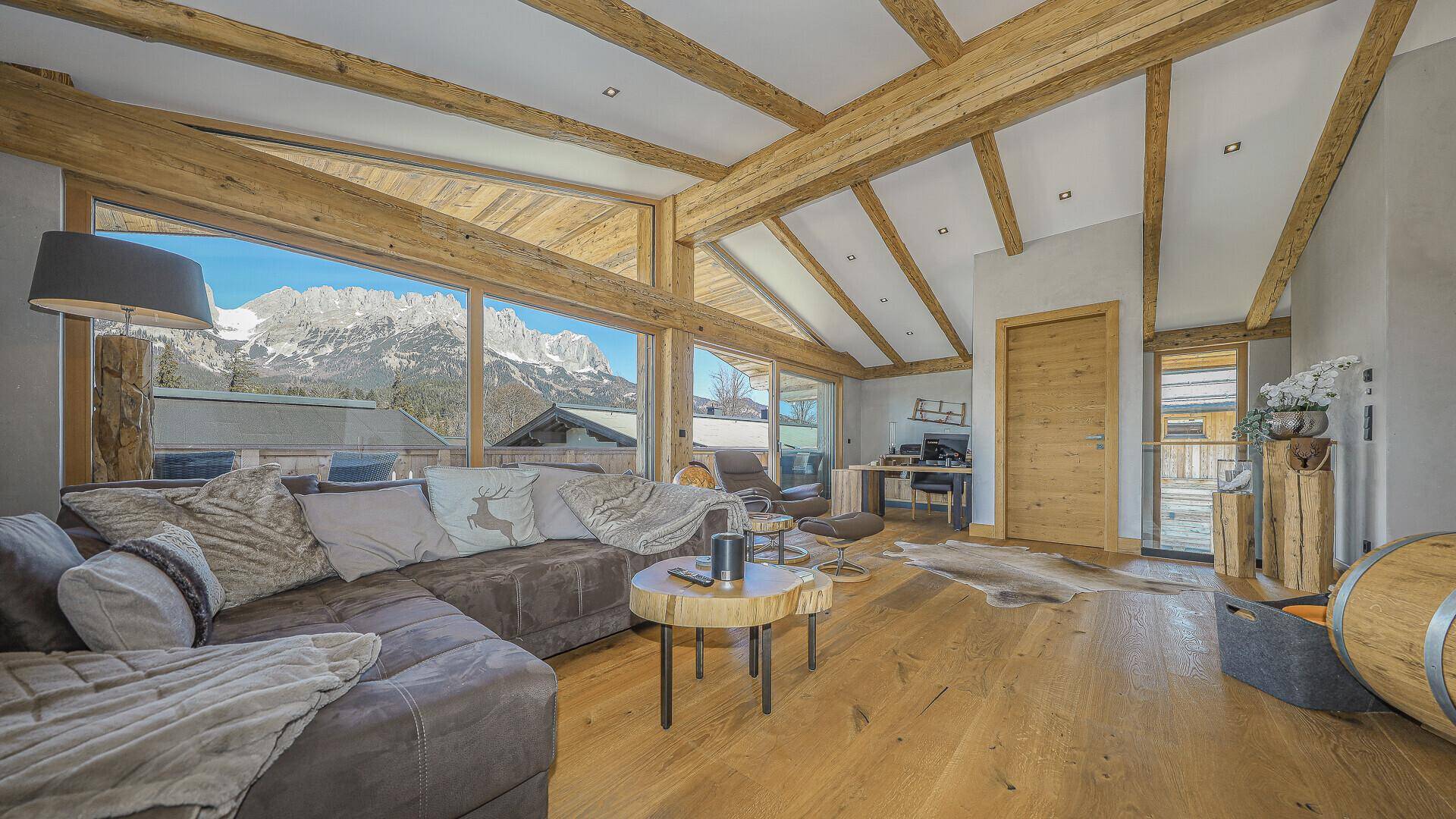 Gemütliches Wohnzimmer mit Holzbalken, Parkettboden und Panoramafenstern mit Bergblick.