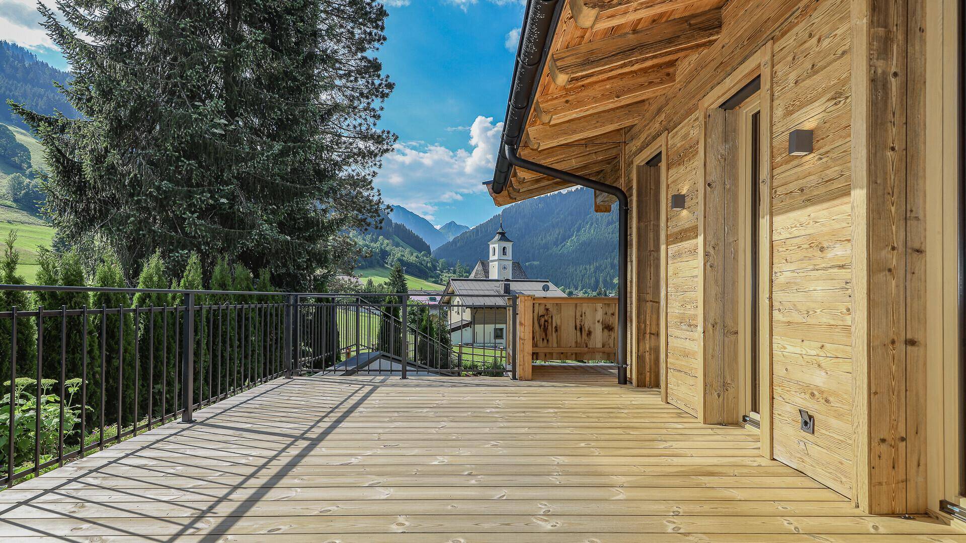 Geräumiger Holzbalkon mit Metallgeländer und malerischem Blick auf die Berglandschaft und das Dorf.