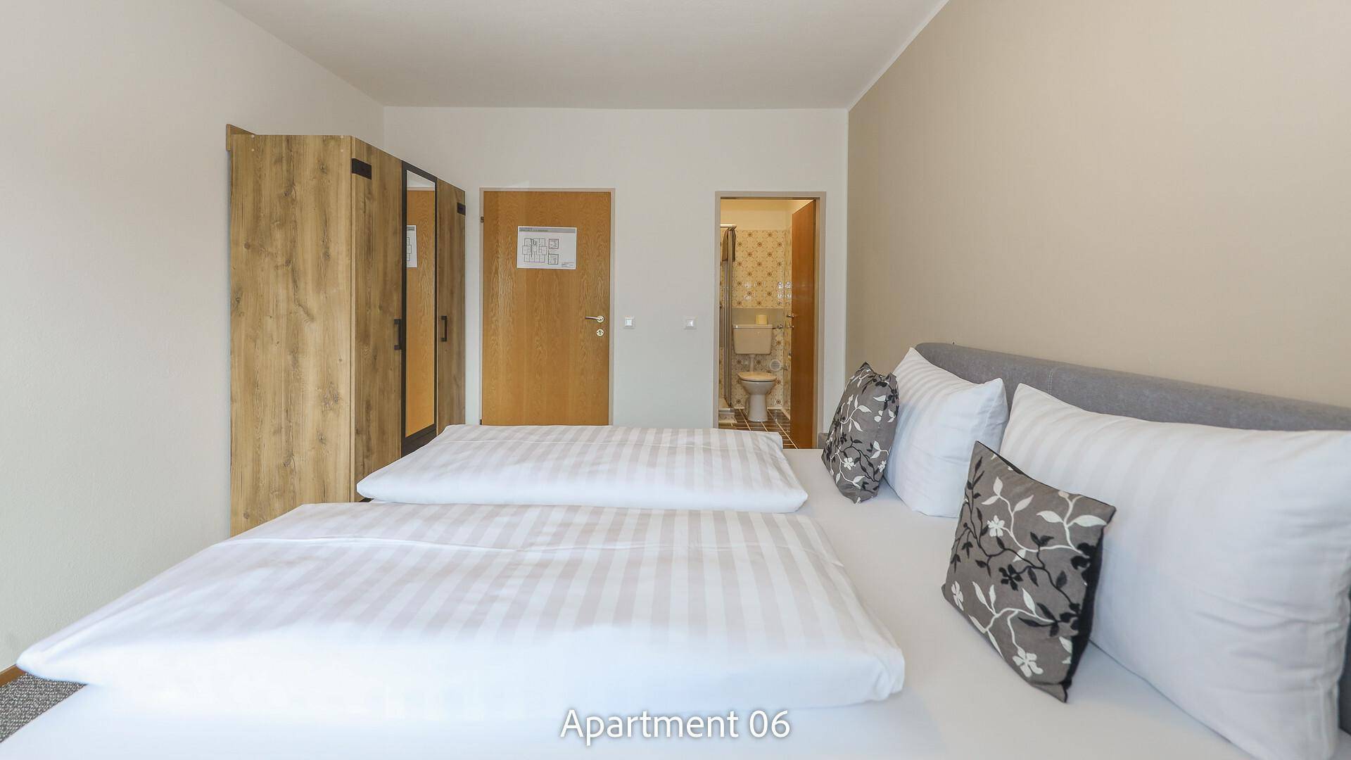 Helles Schlafzimmer von Apartment 06 mit Doppelbett und Zugang zum Badezimmer.