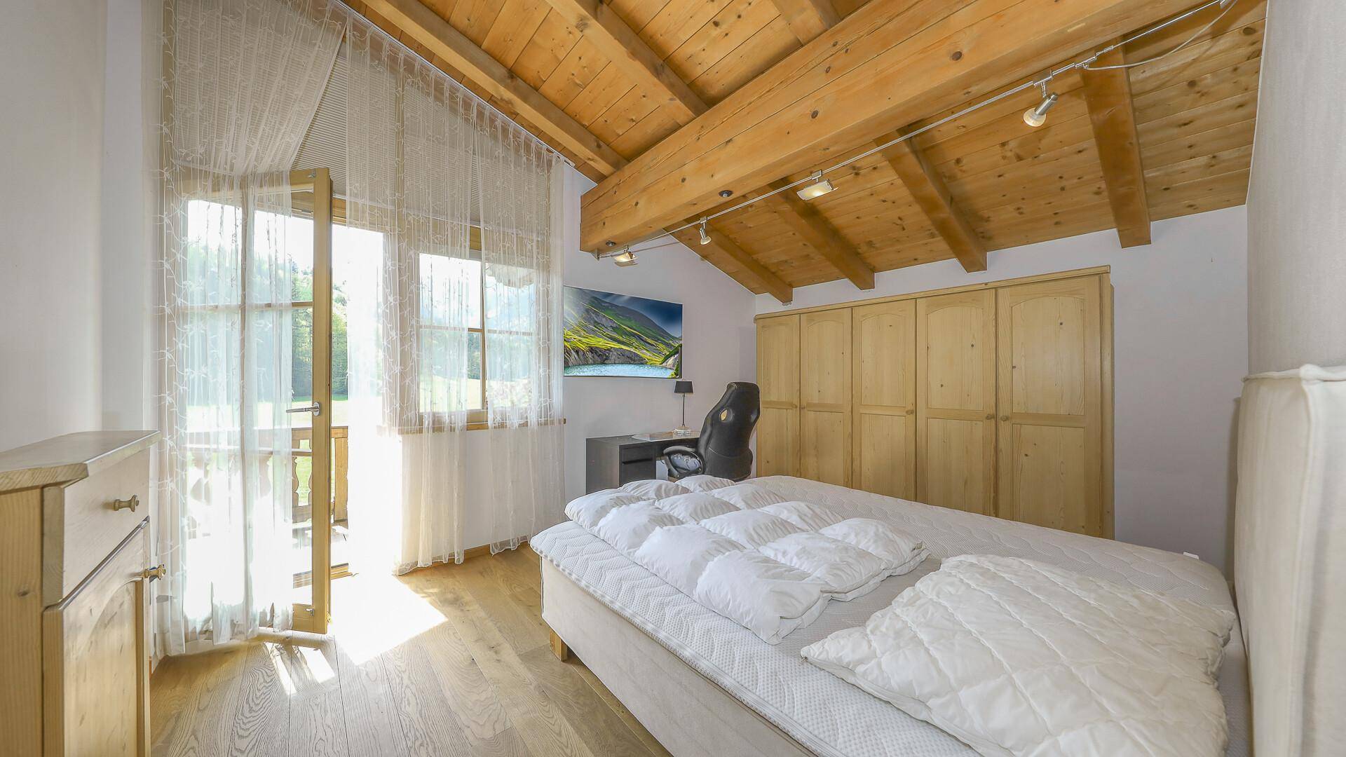 Schlafzimmer mit Einbauschränken, Holzboden und Zugang zu einem sonnigen Balkon.