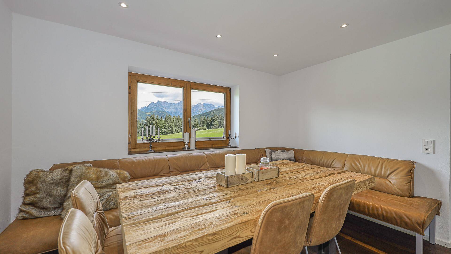 Rustikaler Essbereich mit Holztisch, bequemer Eckbank und weitem Bergblick durch das Fenster.