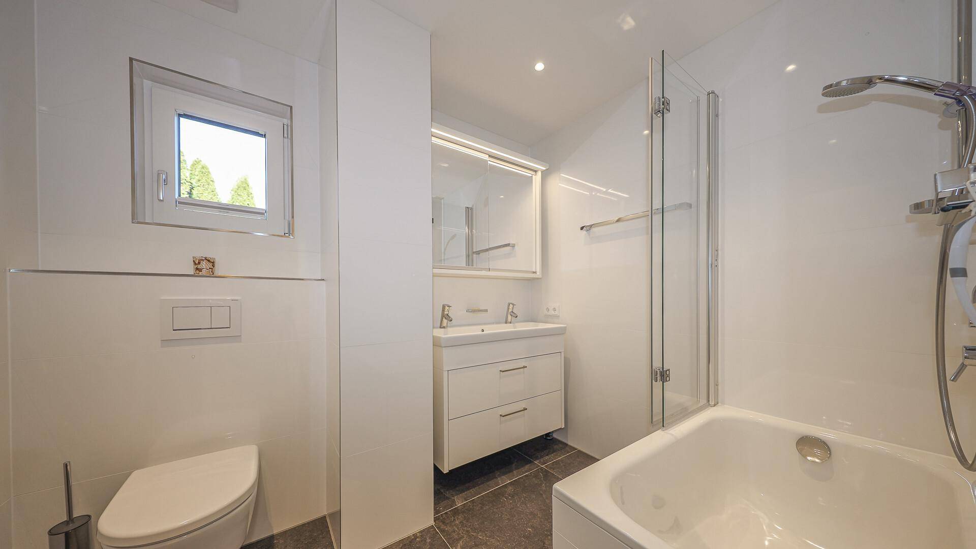 Helles Badezimmer mit Badewanne, Dusche, Waschbecken und Fenster für Tageslicht.