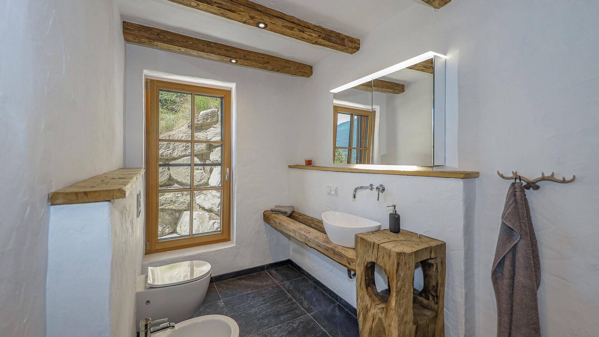 Modernes Badezimmer mit Holzbalken, Natursteinfliesen, Einzelwaschbecken und Fenster.