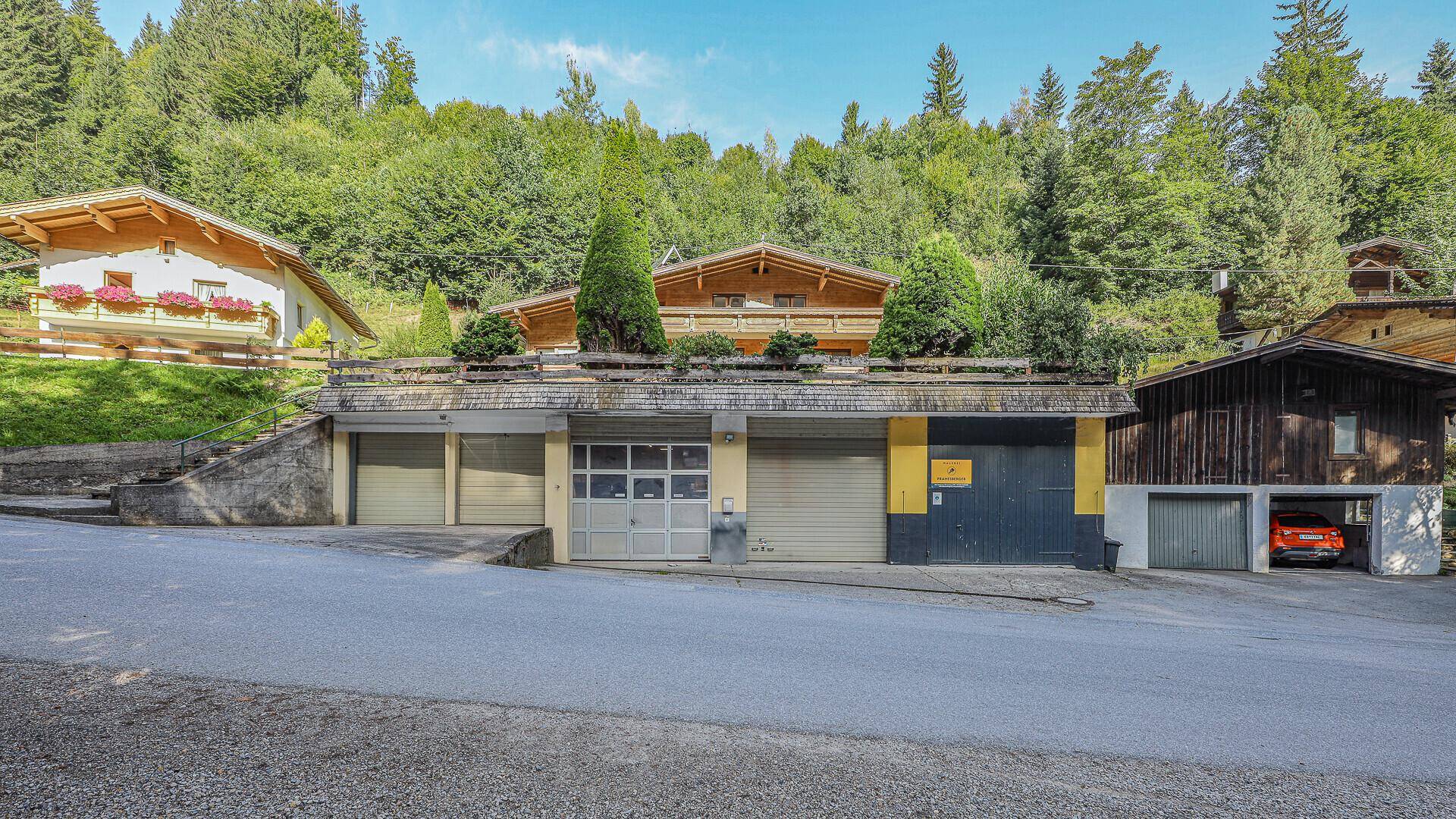Mehrere Garagen und Parkplätze unterhalb eines traditionellen Hauses an einer Straße.