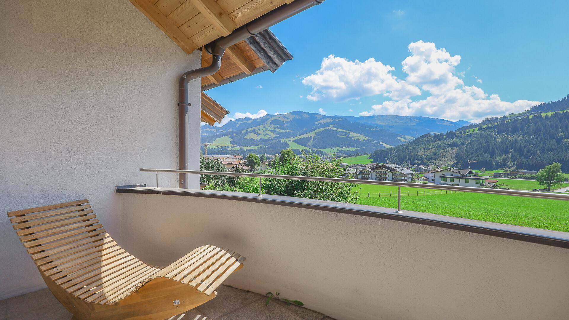 Gemütlicher Balkon mit Holzliege und weitem Blick auf die umliegende Berglandschaft.