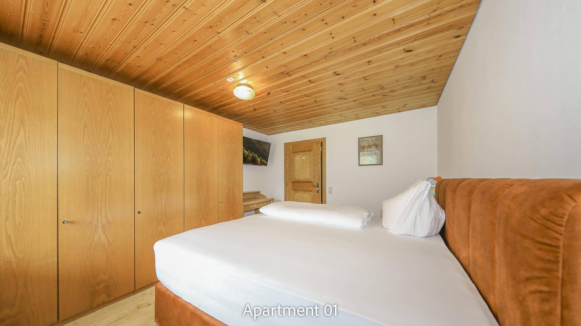 Schlafzimmer von Apartment 01 mit Doppelbett, großem Holzschrank und einer Holzdecke.