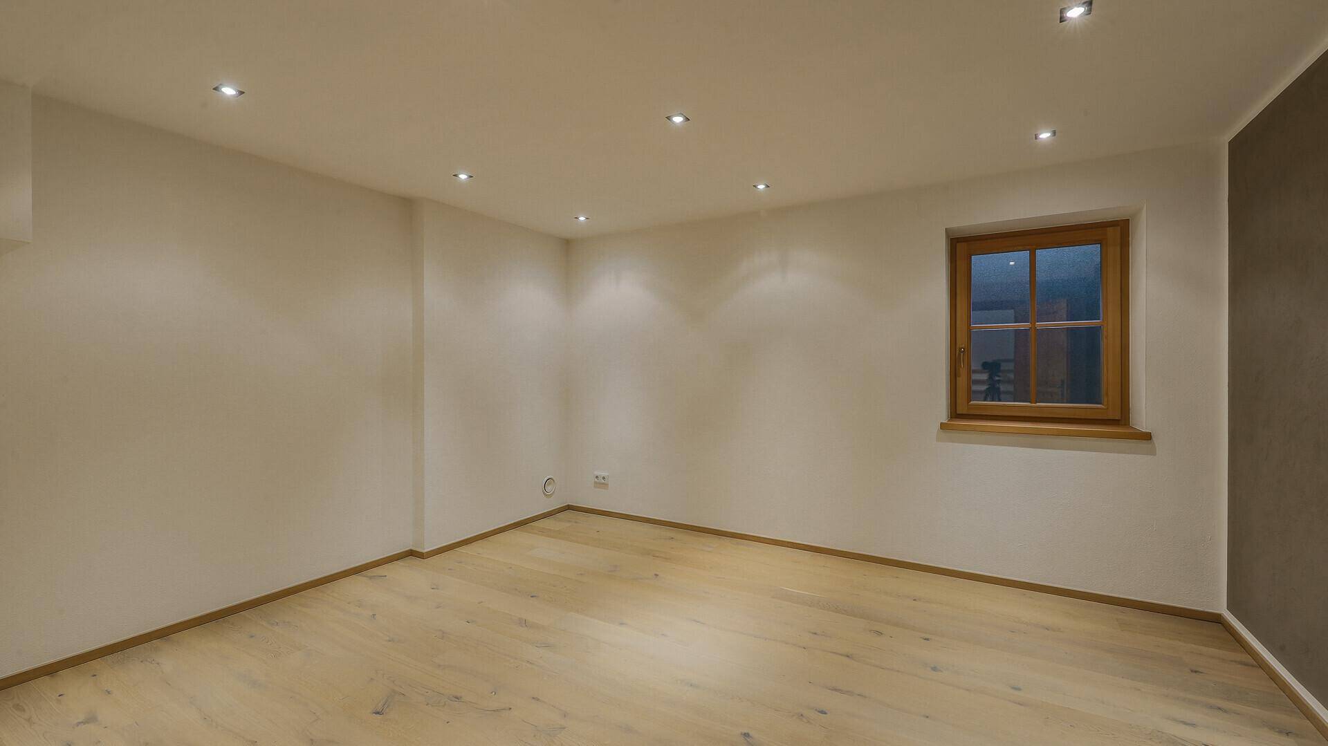 Heller, leerer Raum mit Holzboden, weißen Wänden und einem Fenster.