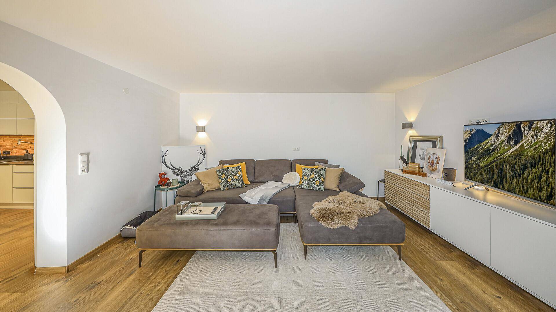 Modernes Wohnzimmer mit großem Ecksofa, Fernseher und stilvoller Dekoration, offen zu einem weiteren Bereich.