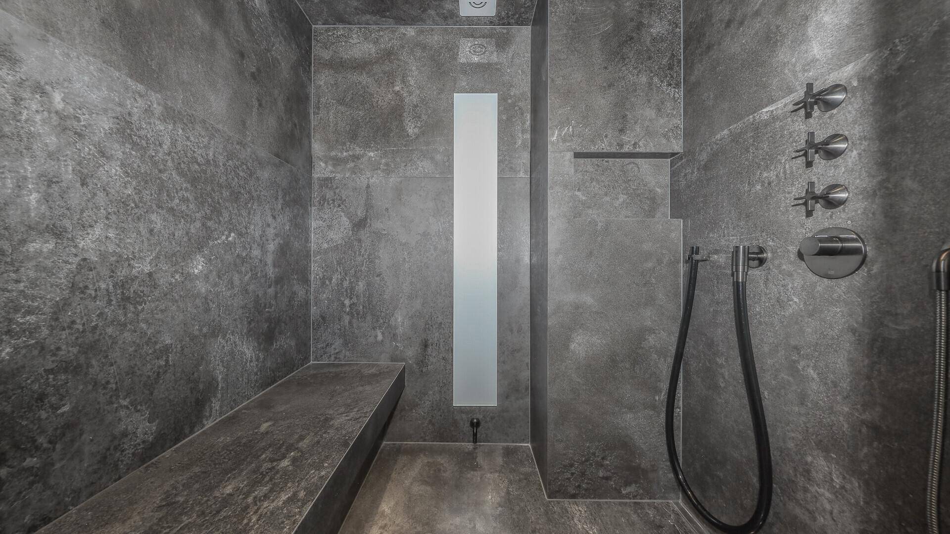 Elegante Dusche mit dunklen Fliesen und integrierter Sitzbank im modernen Design.