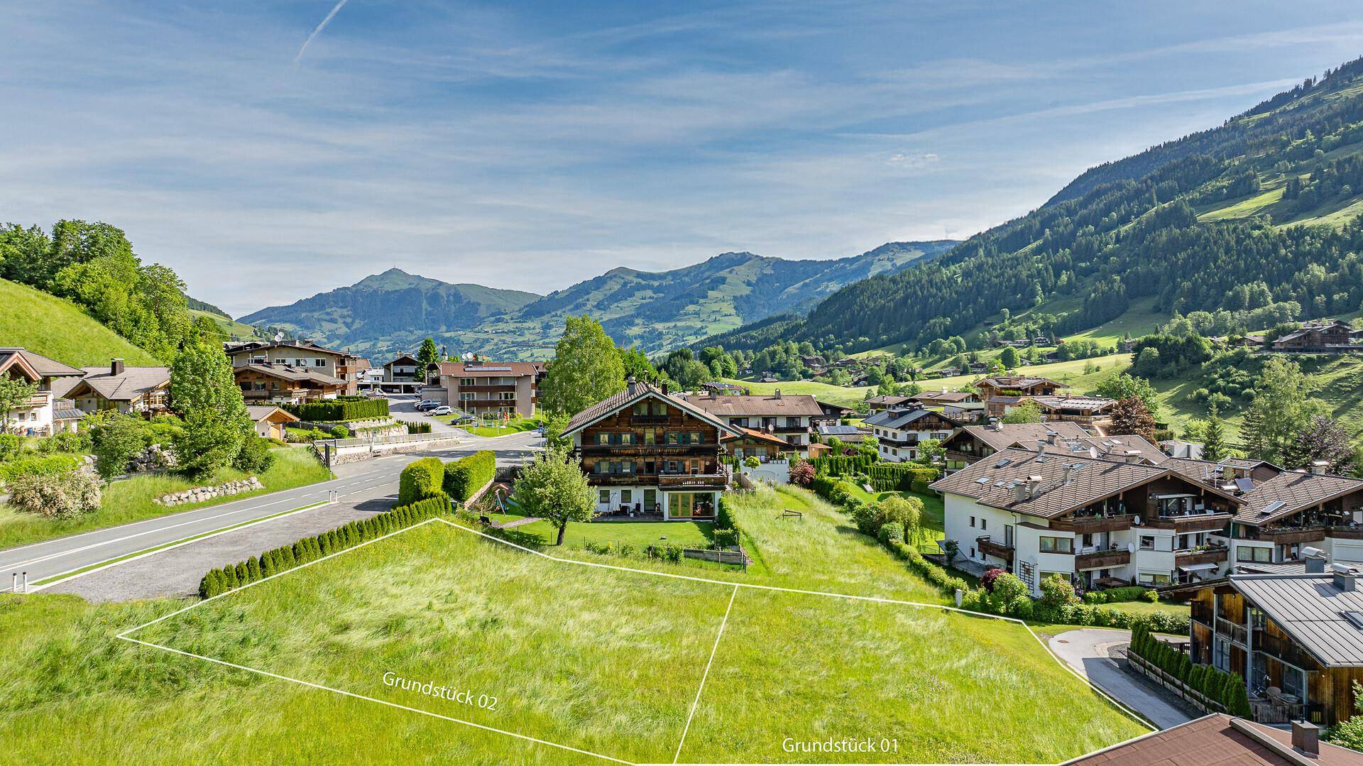 Luftaufnahme eines Dorfes in den Bergen mit zwei markierten Grundstücken und grünen Wiesen.