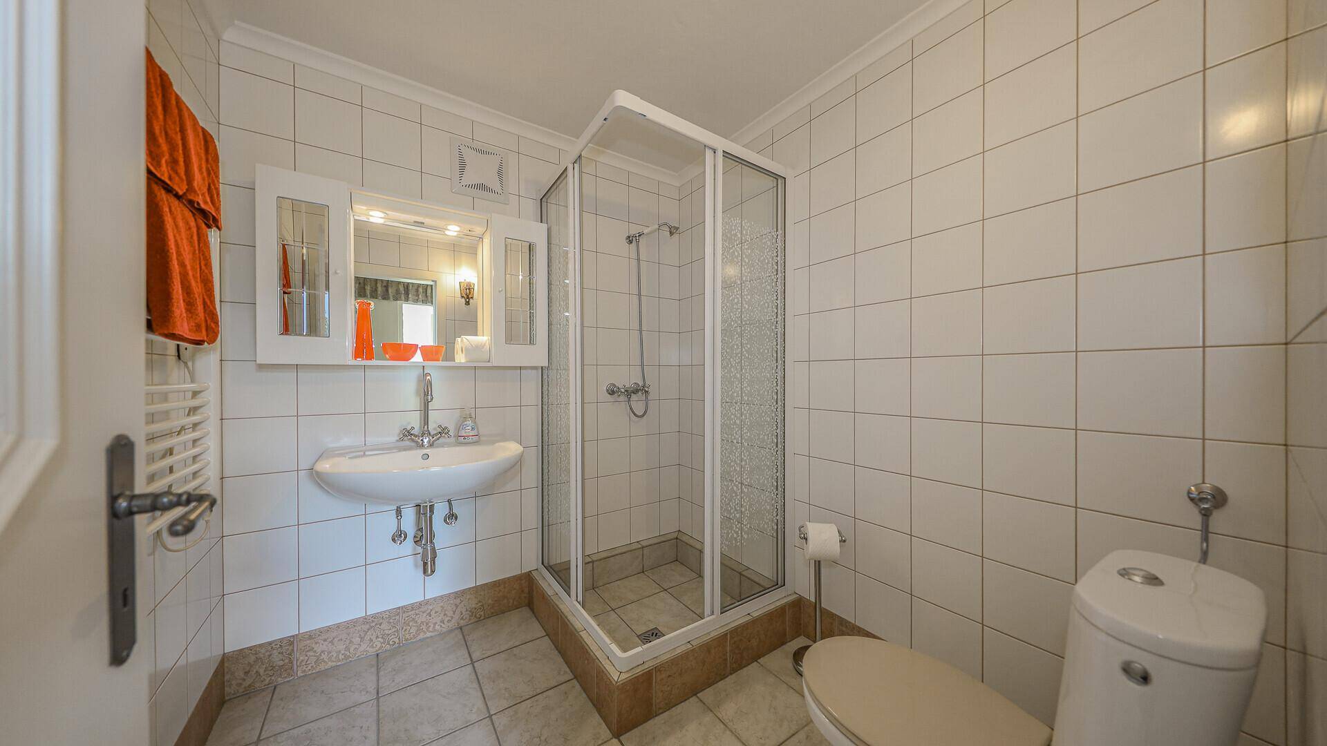 Badezimmer mit weißen Fliesen, Duschkabine, Waschbecken und Spiegelschrank.