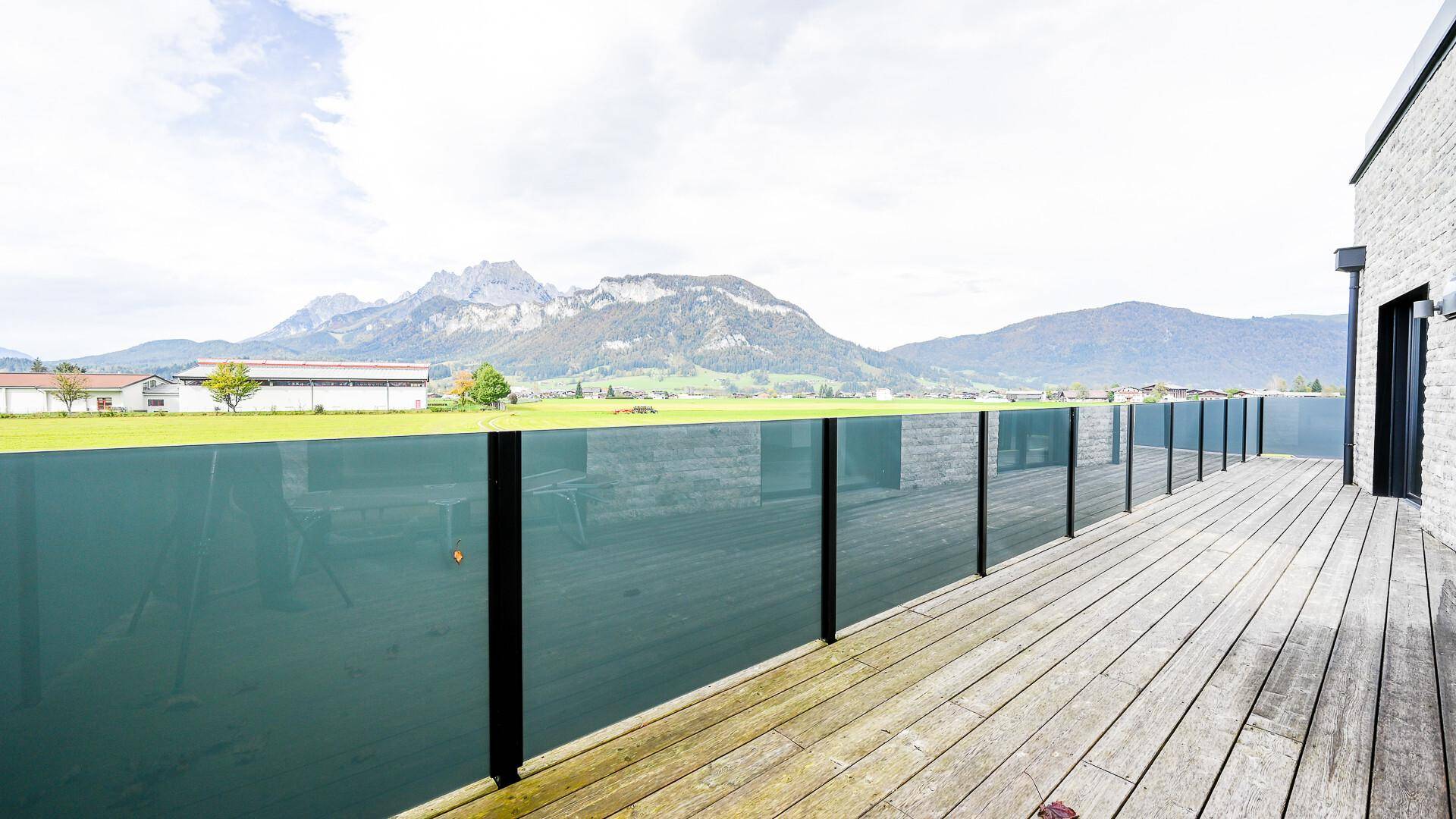Große Holzterrasse mit Glasgeländer und Panoramablick auf die umliegende Berglandschaft.