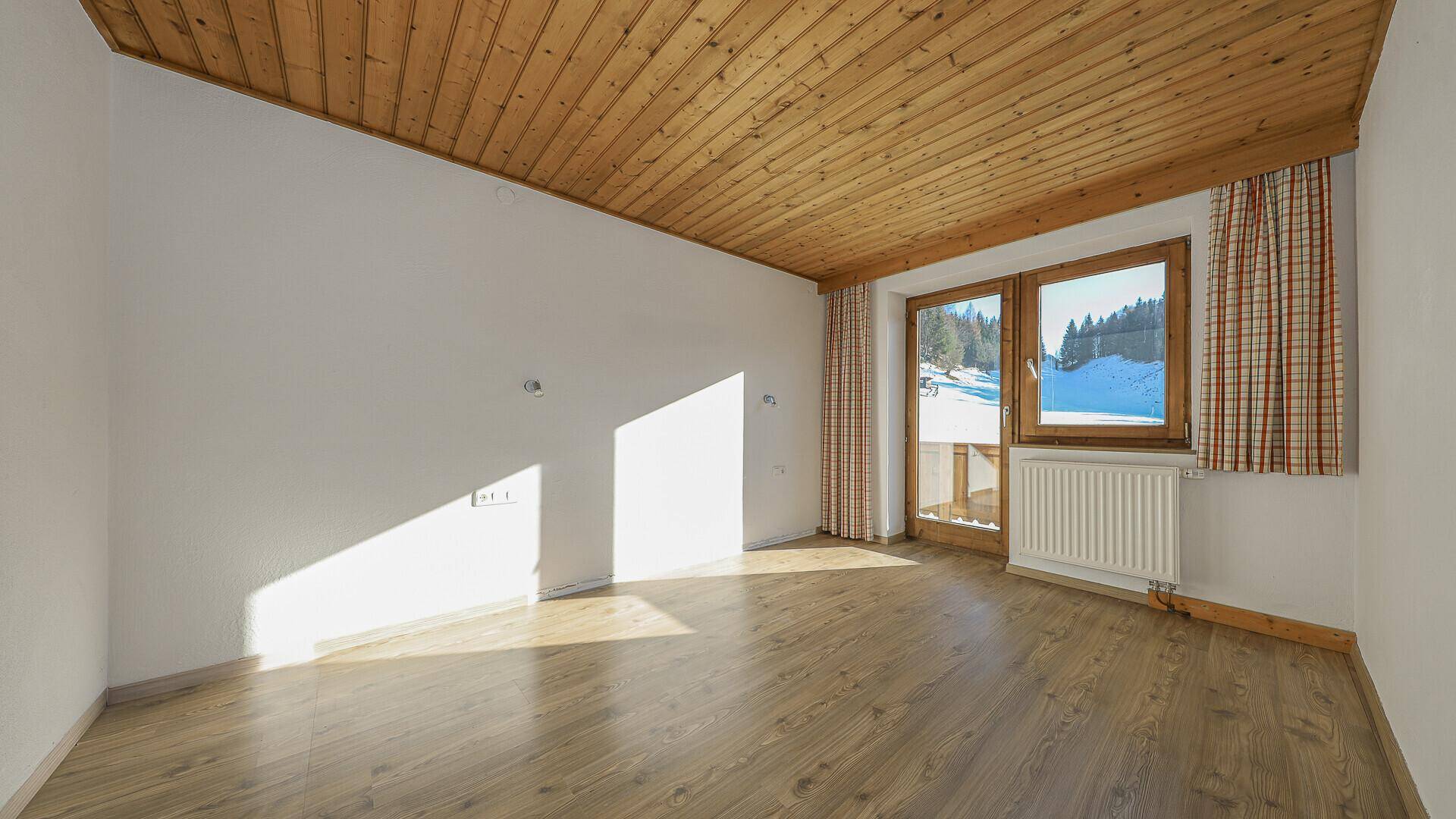 Helles Zimmer mit Holzboden, Holzdecke und Blick auf die verschneite Landschaft.