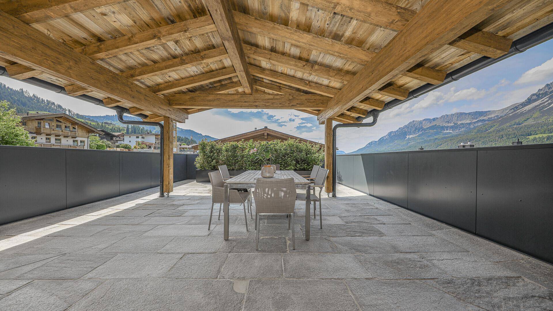 Überdachte Terrasse mit Esstisch und Stühlen, ideal für Mahlzeiten im Freien mit Bergblick.