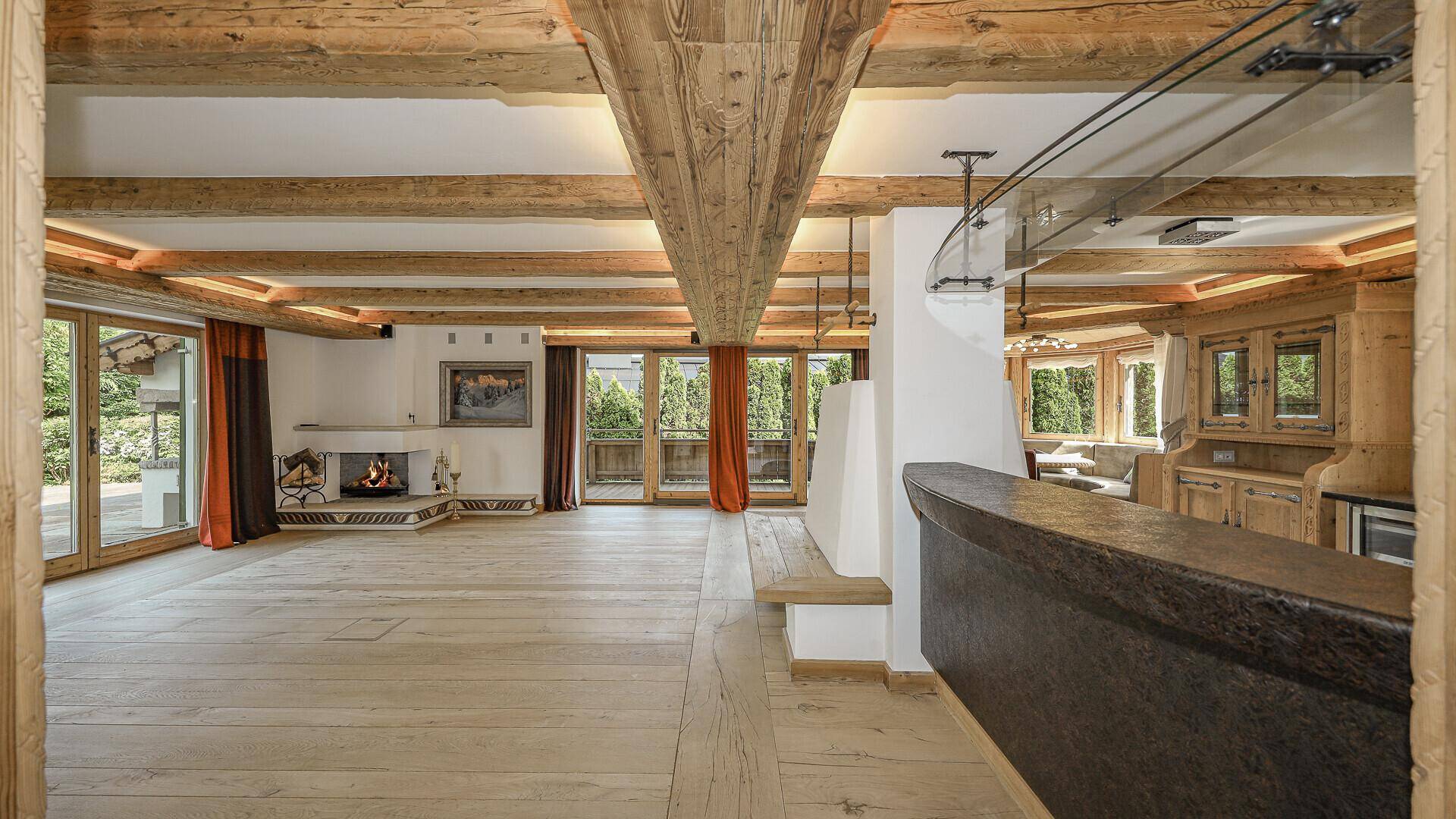 Geräumiges Wohnzimmer im alpinen Stil mit Holzbalken, Kamin und Barbereich.