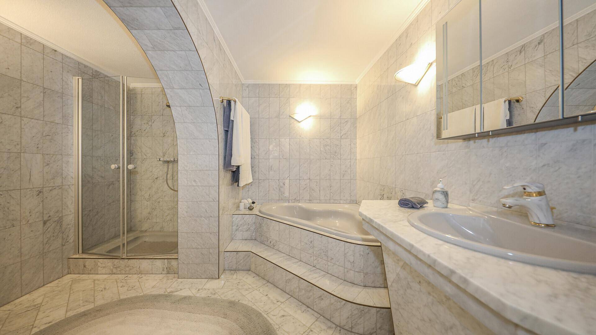 Geräumiges Badezimmer mit Marmorfliesen, Badewanne und separater Duschkabine.