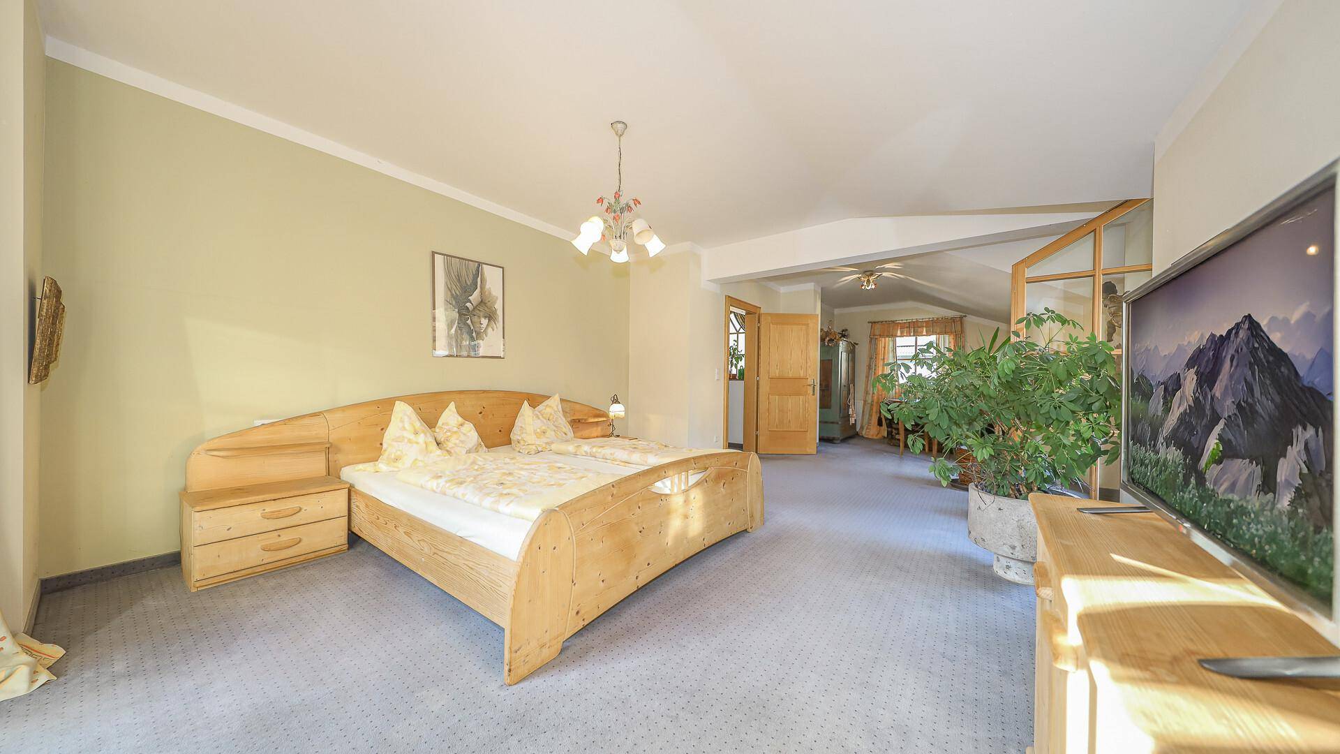 Großes Schlafzimmer mit Doppelbett, Teppichboden und Blick in den angrenzenden Bereich.